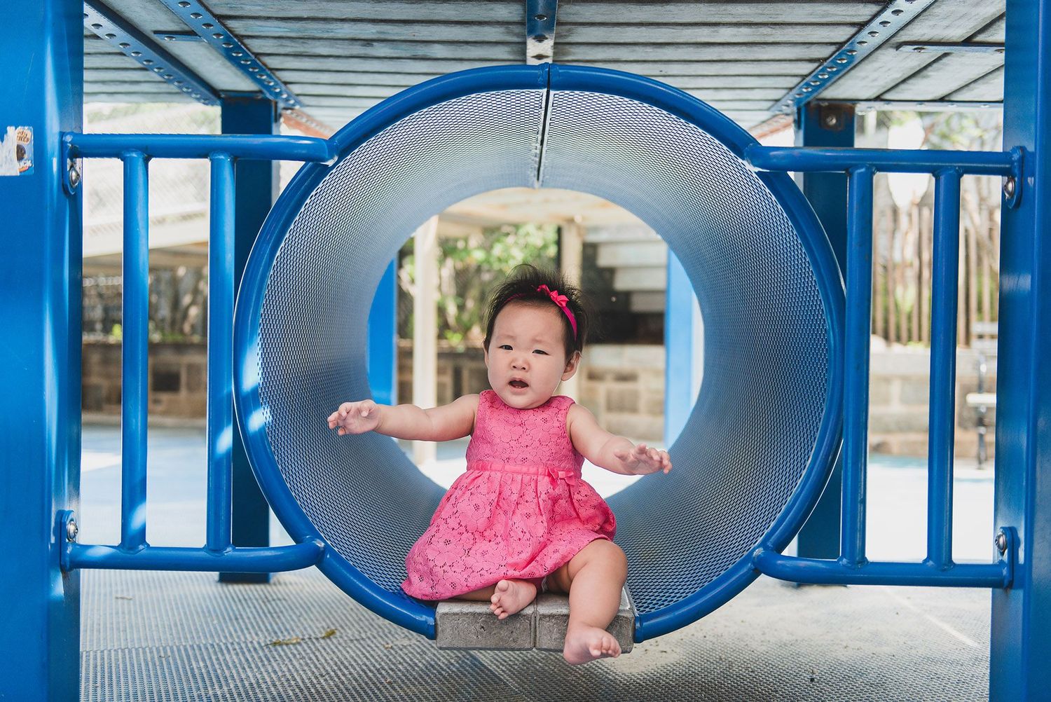 Child playing in blue playground tunnel equipment during sunny day.
