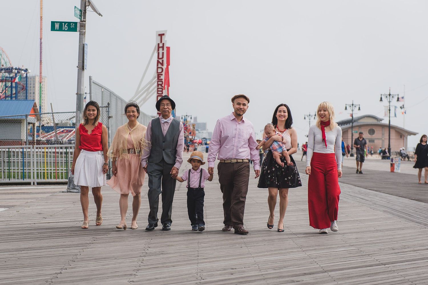 Group walking along boardwalk near beach with buildings in background.