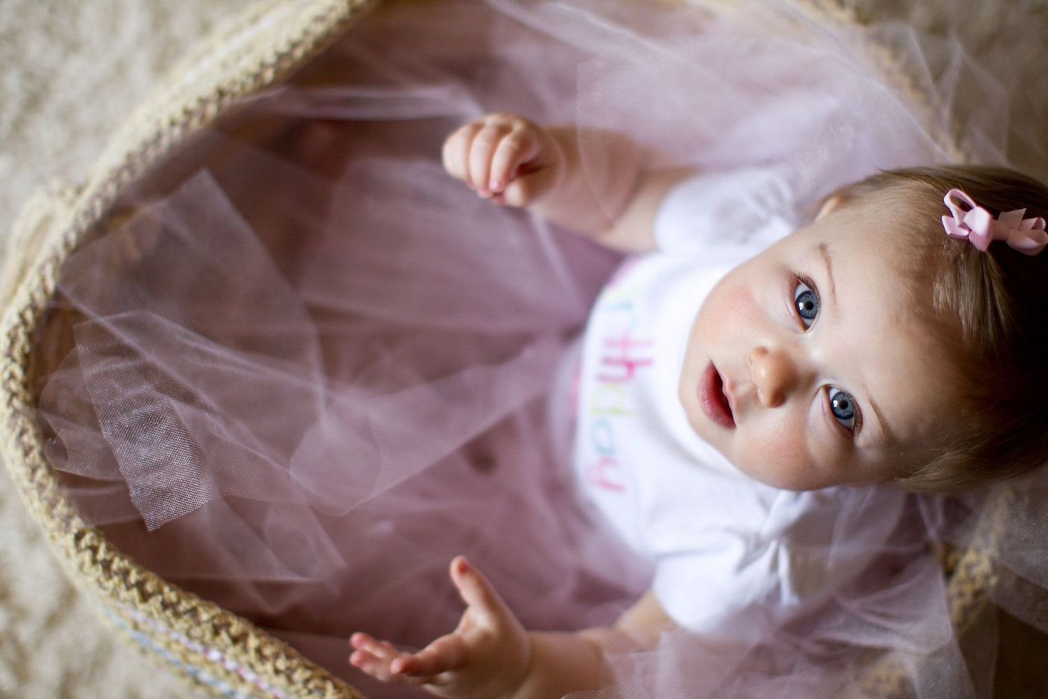 Baby wearing pink tulle dress lies on soft white fabric in dreamy portrait setting.