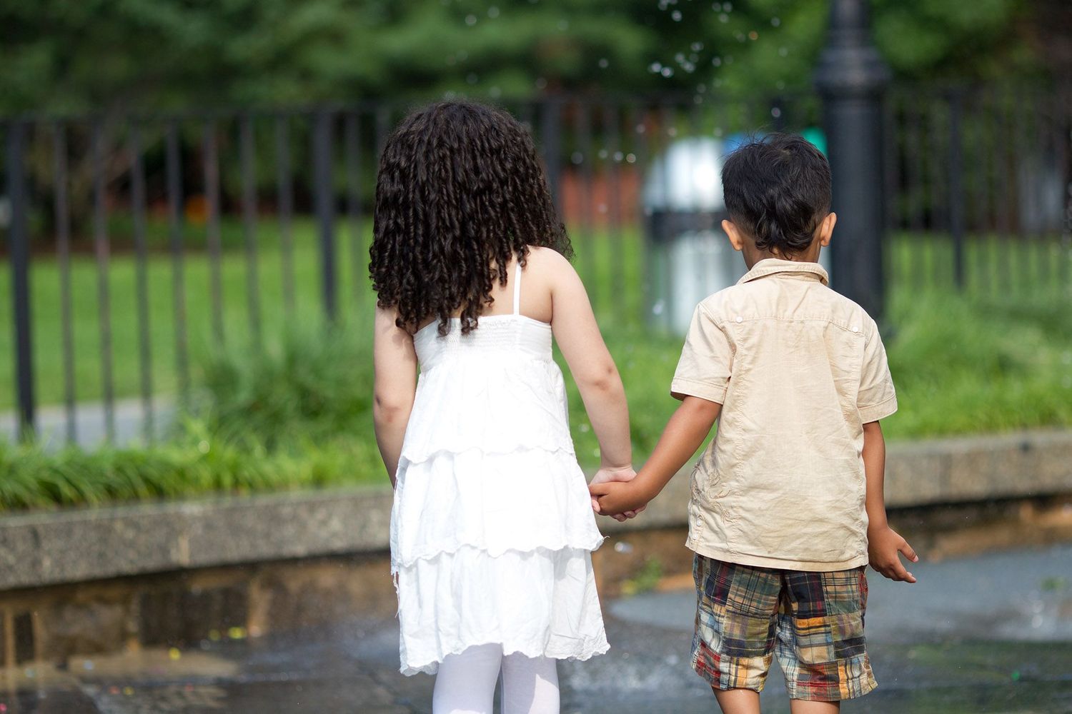 Children walking hand in hand through park on summer day.