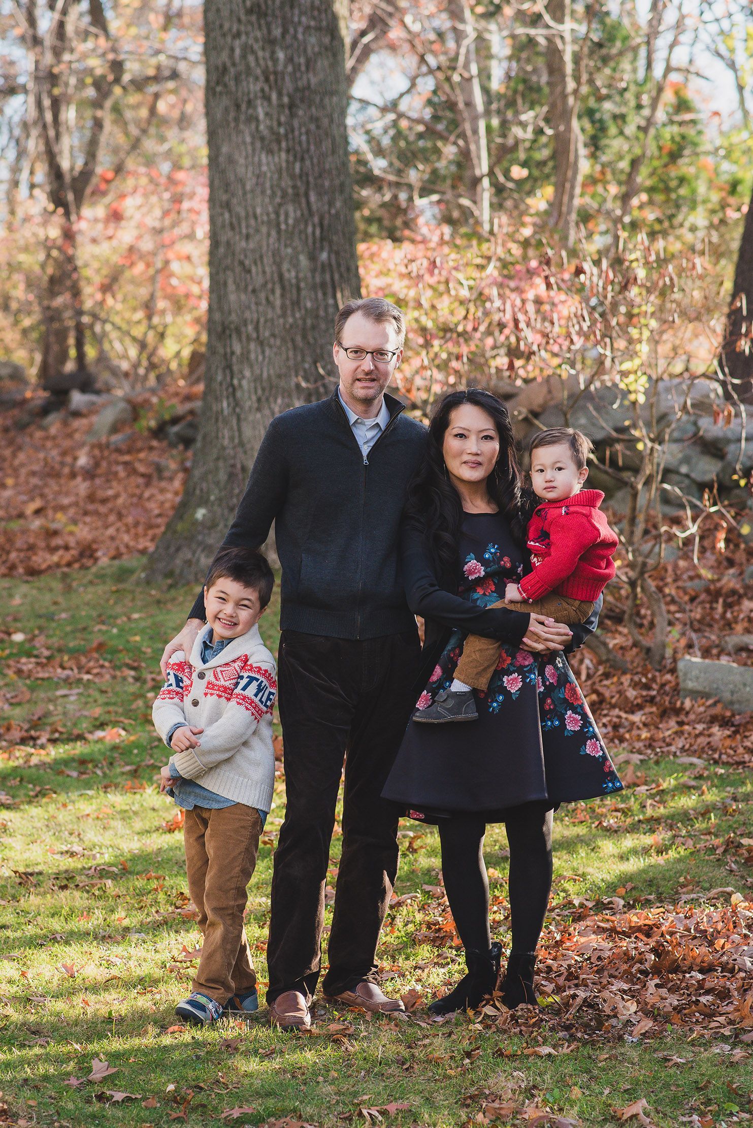 Family group poses together on fallen autumn leaves in a park setting.
