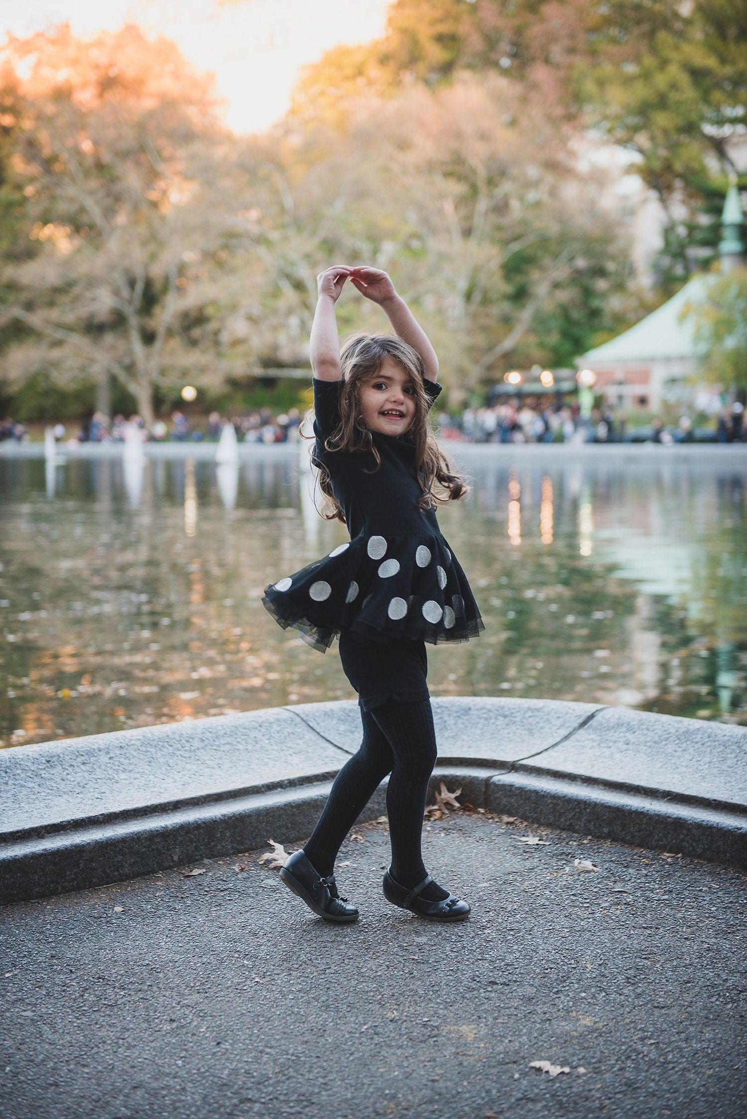 Young dancer in polka dot dress performing by lake during autumn sunset.