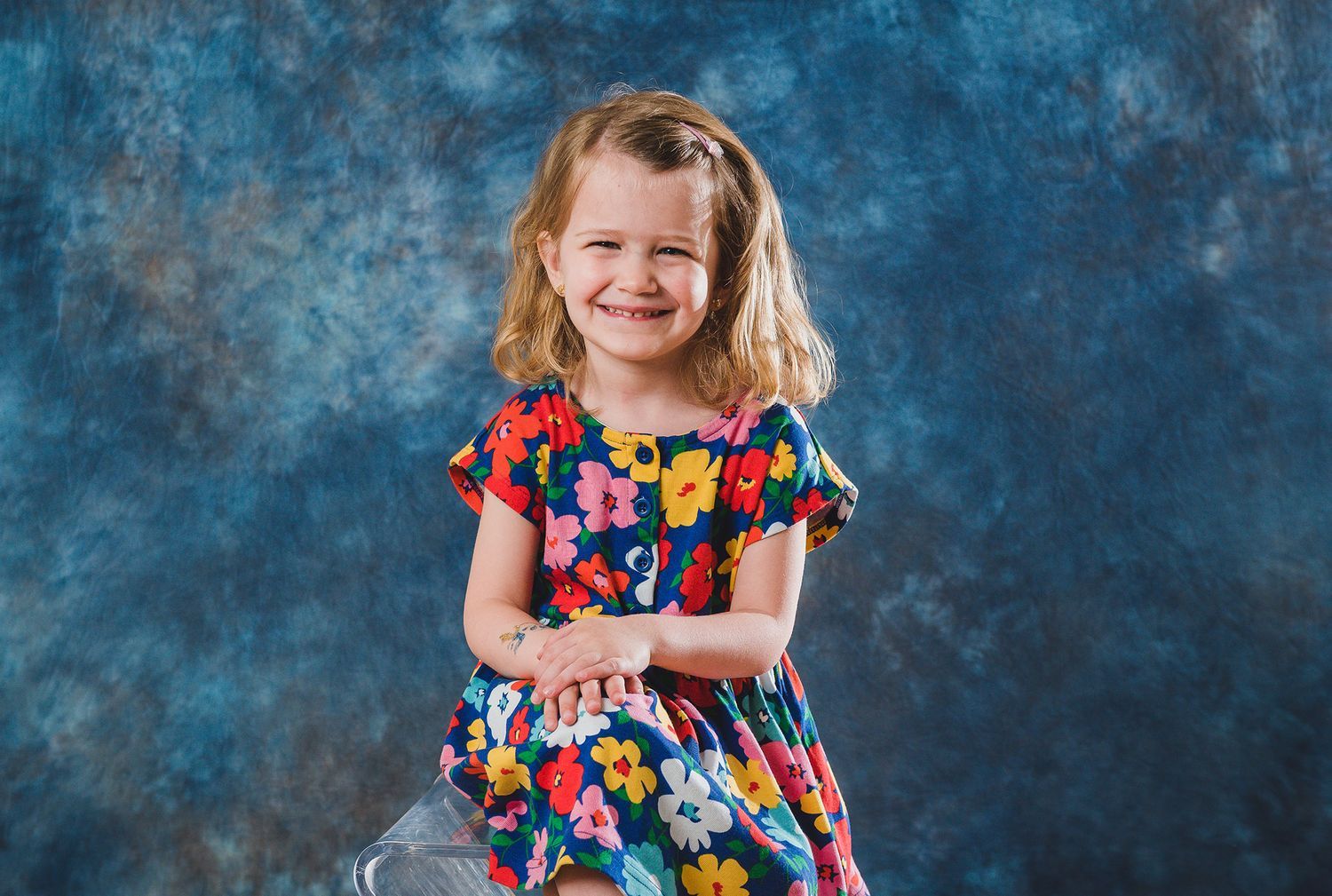 Child in colorful floral dress posing against blue textured background.