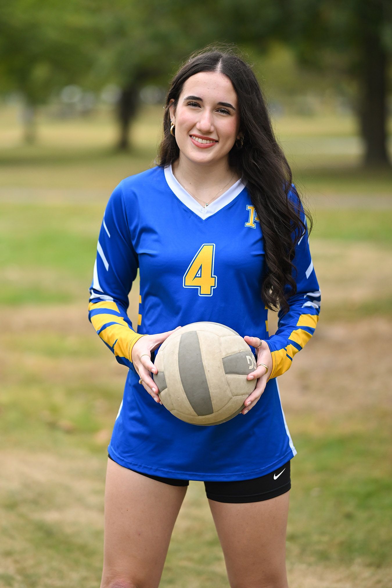 Volleyball player in blue and yellow jersey number 4 holding volleyball outdoors.
