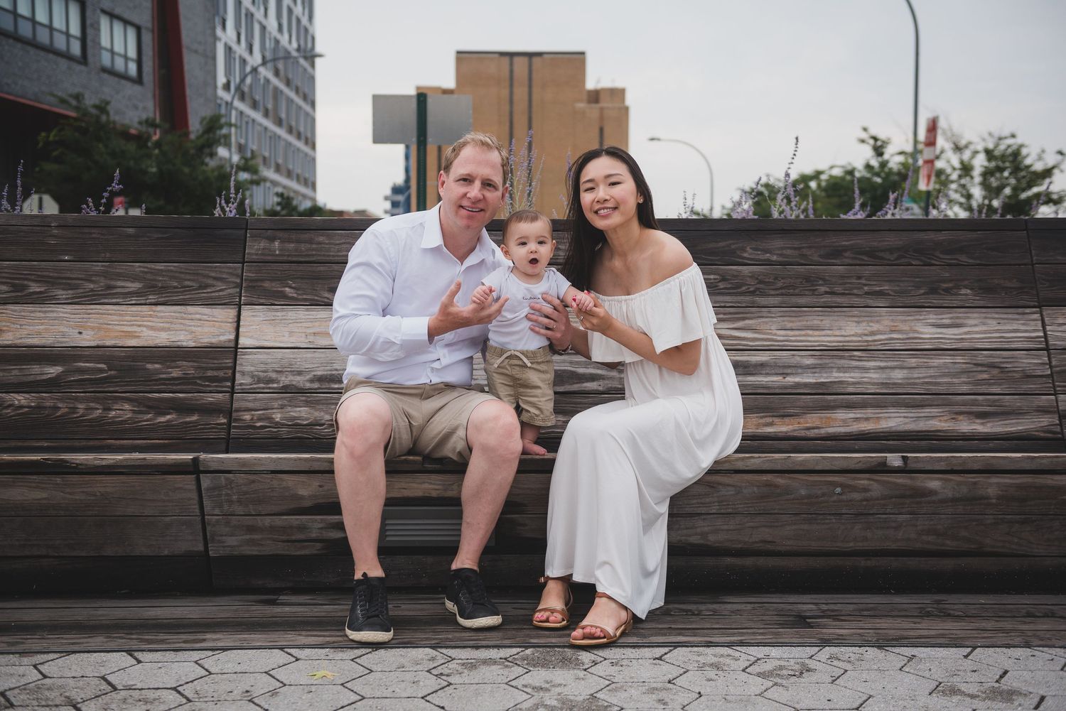 Family sitting on wooden bench against urban backdrop during photo session.