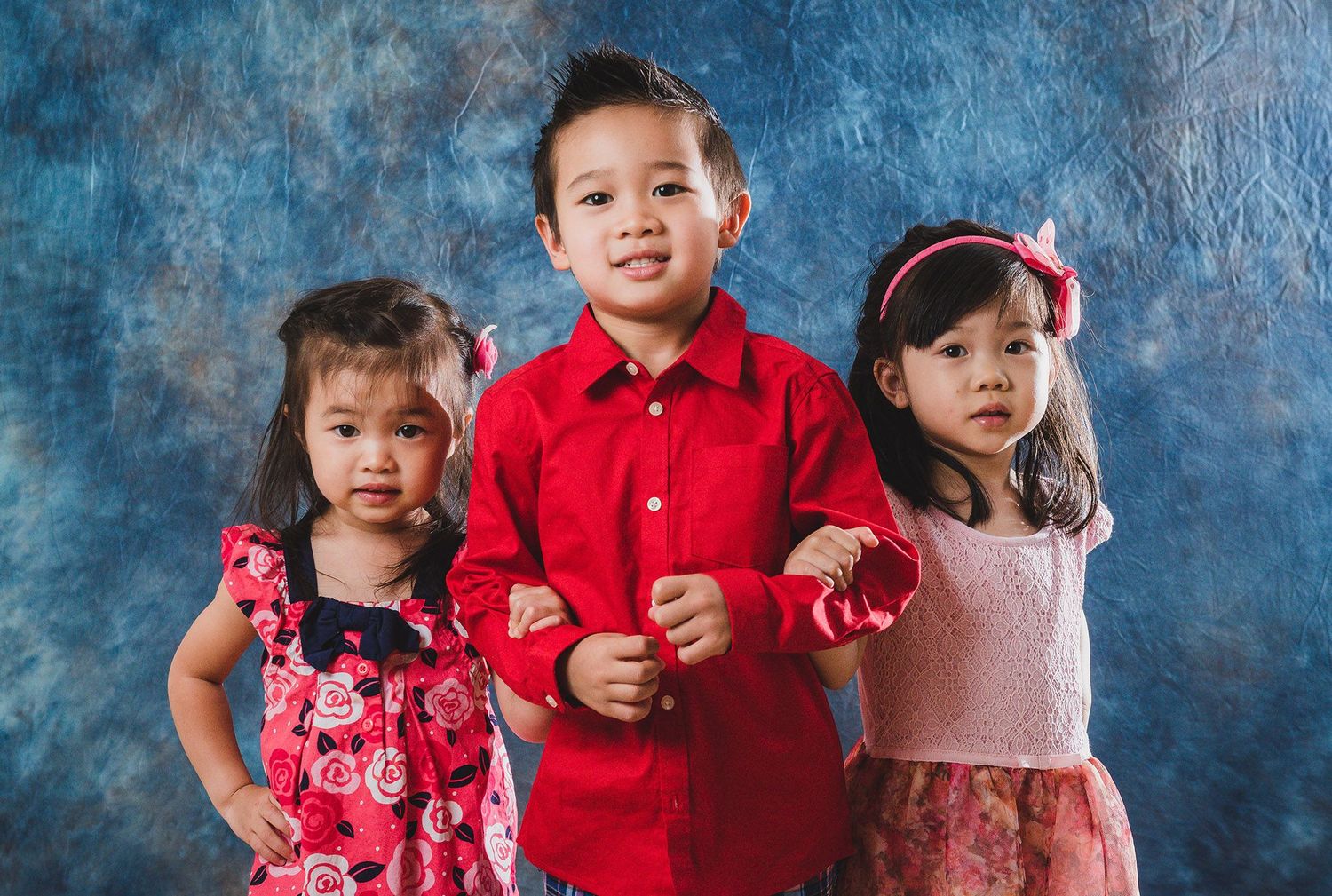 Group of children in red and pink outfits posing together against a blue textured background.