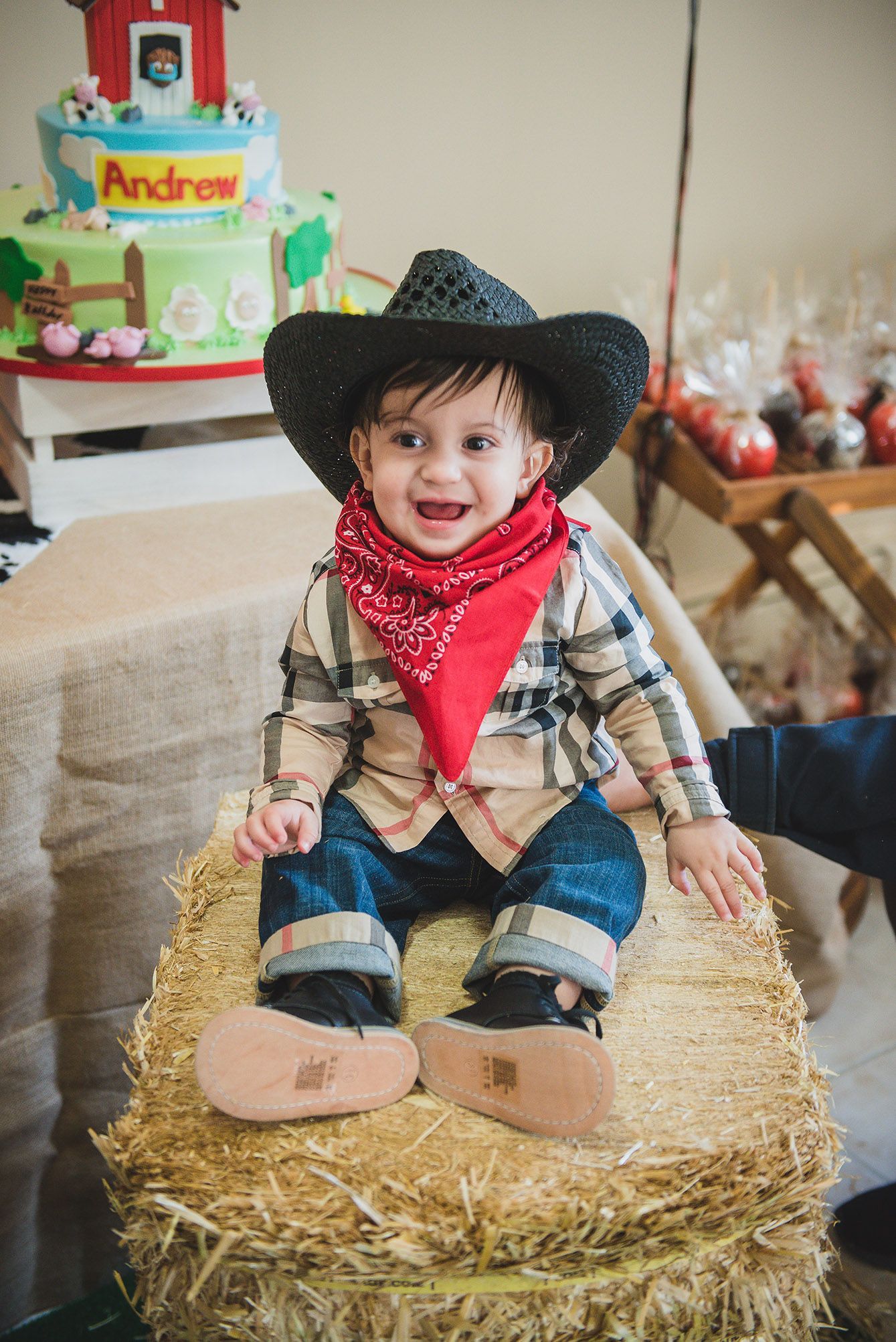 Small child dressed as a cowboy sitting on hay bale wearing denim and red bandana.