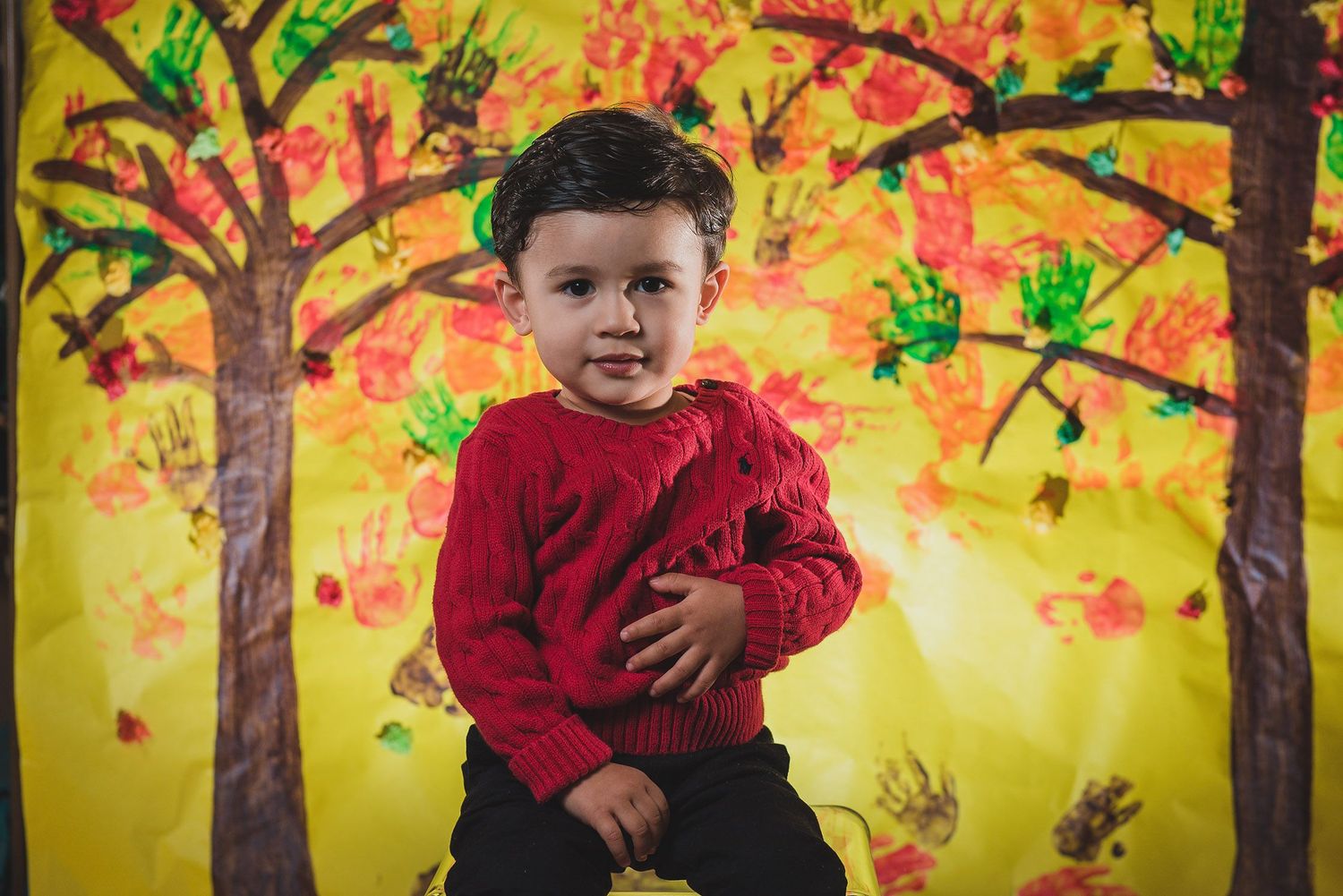 Artistic backdrop with painted fall trees and handprint leaves in vibrant yellow and orange.