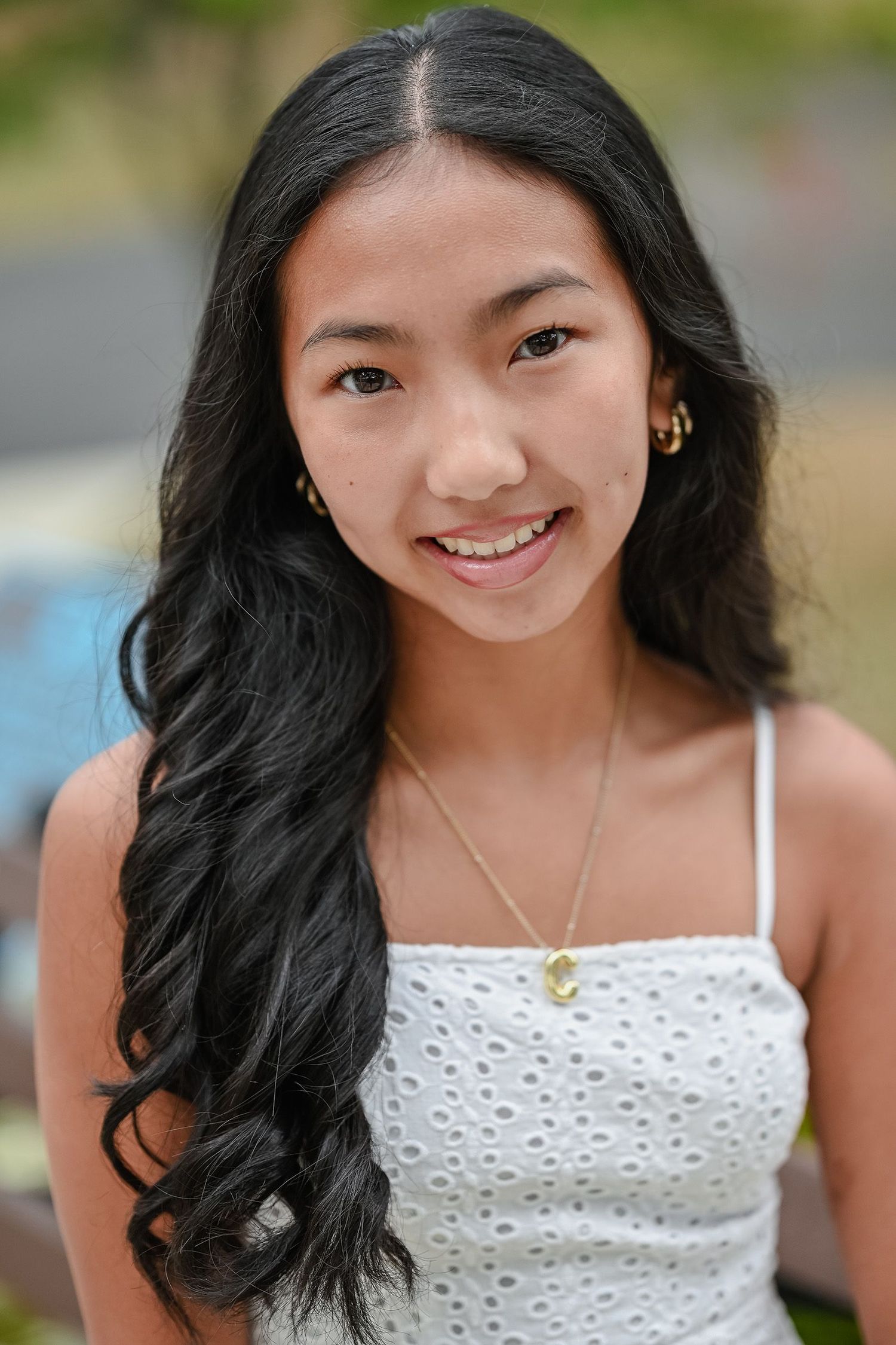 Portrait of young woman with long dark hair wearing white eyelet top with delicate necklace.