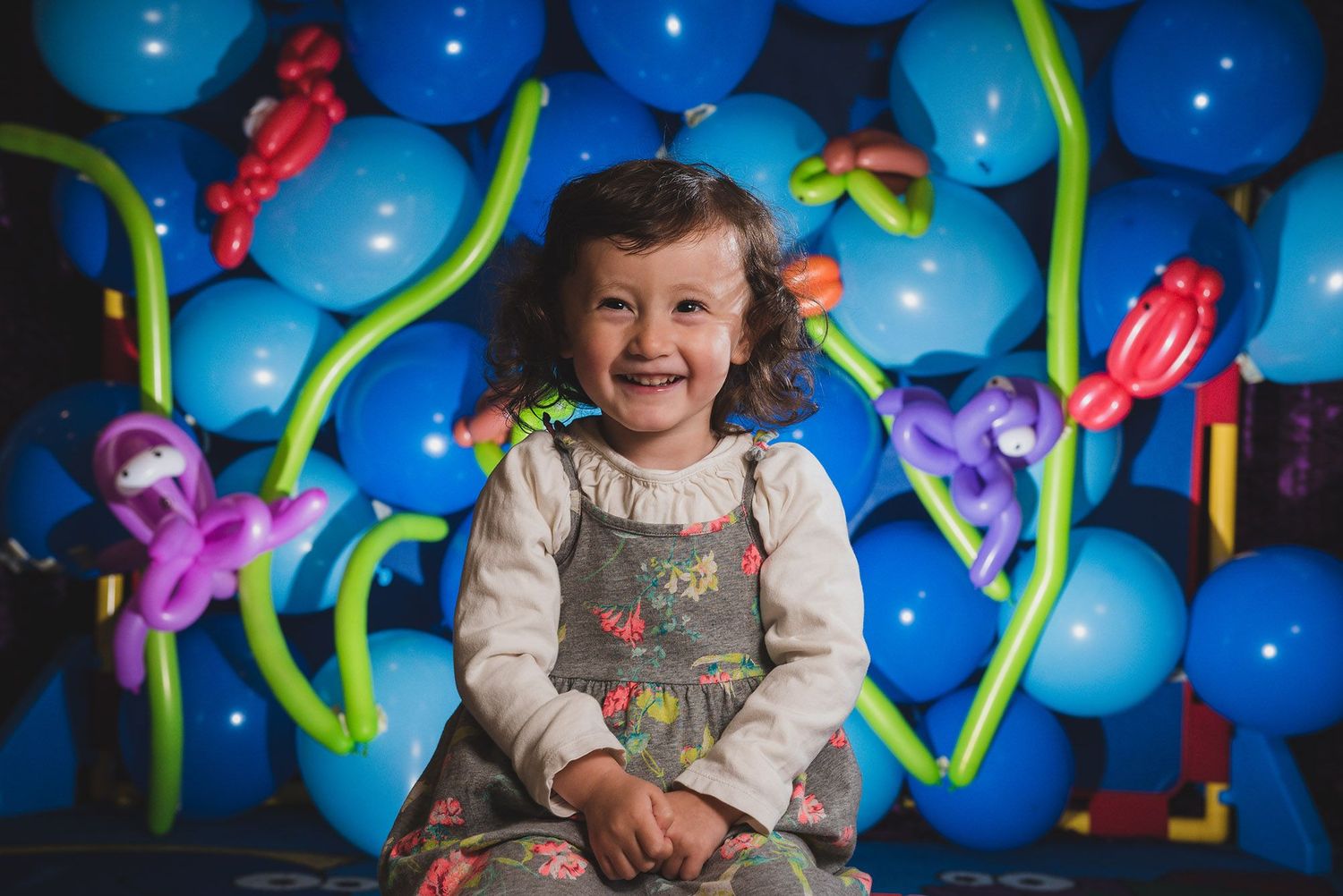 Child poses with balloon decorations and colorful twisted designs against blue background.