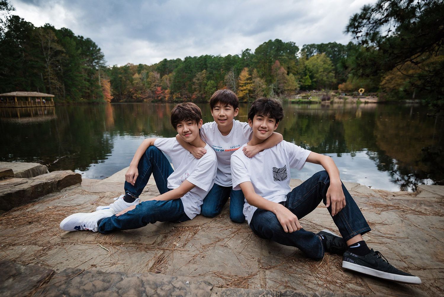 Family relaxing together on rocky outcrop by serene lake during outdoor photoshoot.