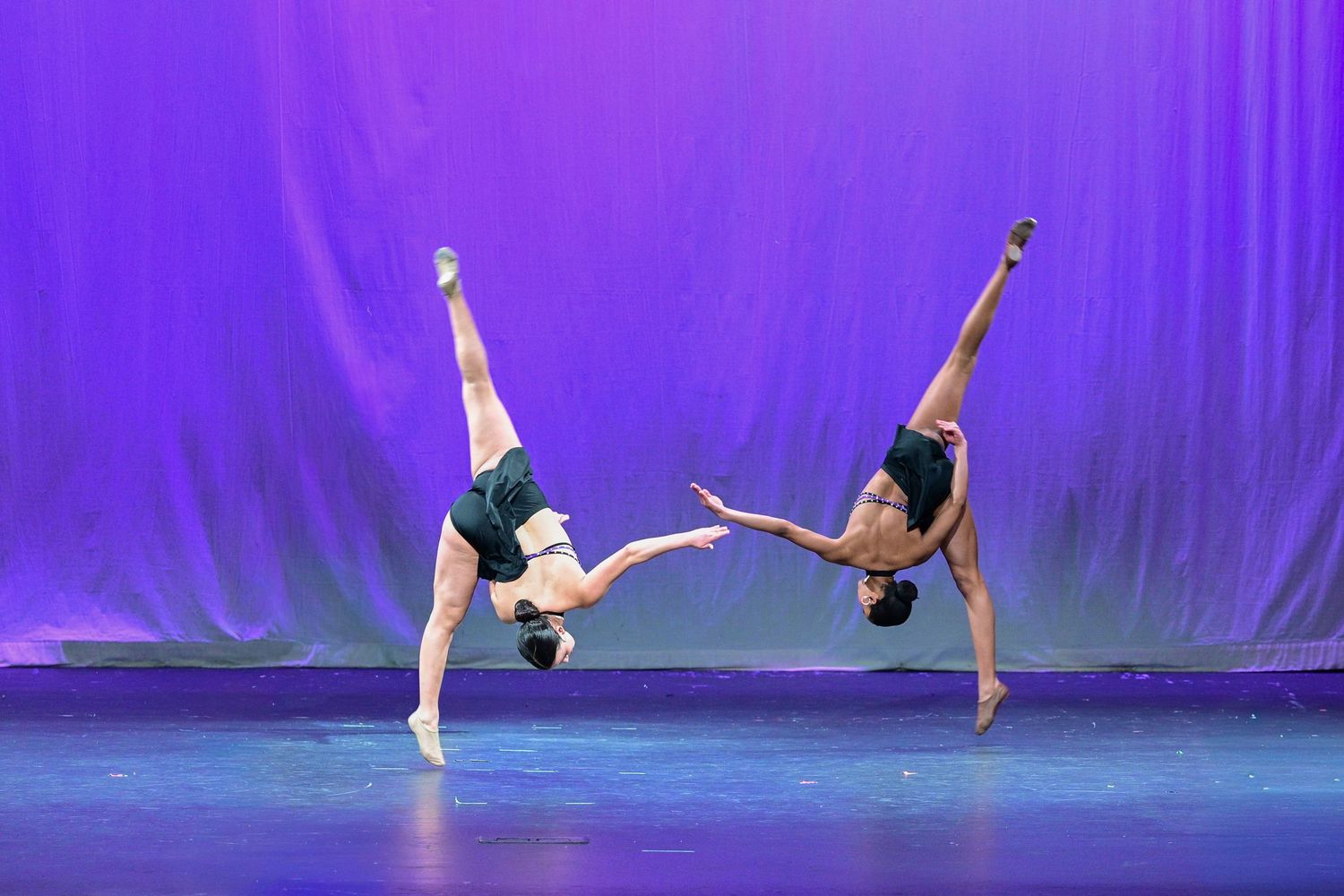 Ballet dancers perform graceful poses and movements on stage against a vibrant purple backdrop.