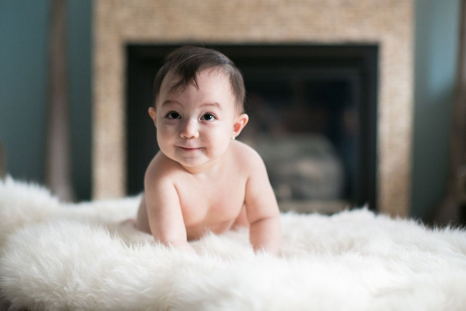 Baby lying on soft white fur blanket in indoor portrait setting.