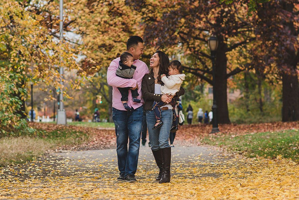 Family walking together through park with golden autumn leaves scattered on ground.