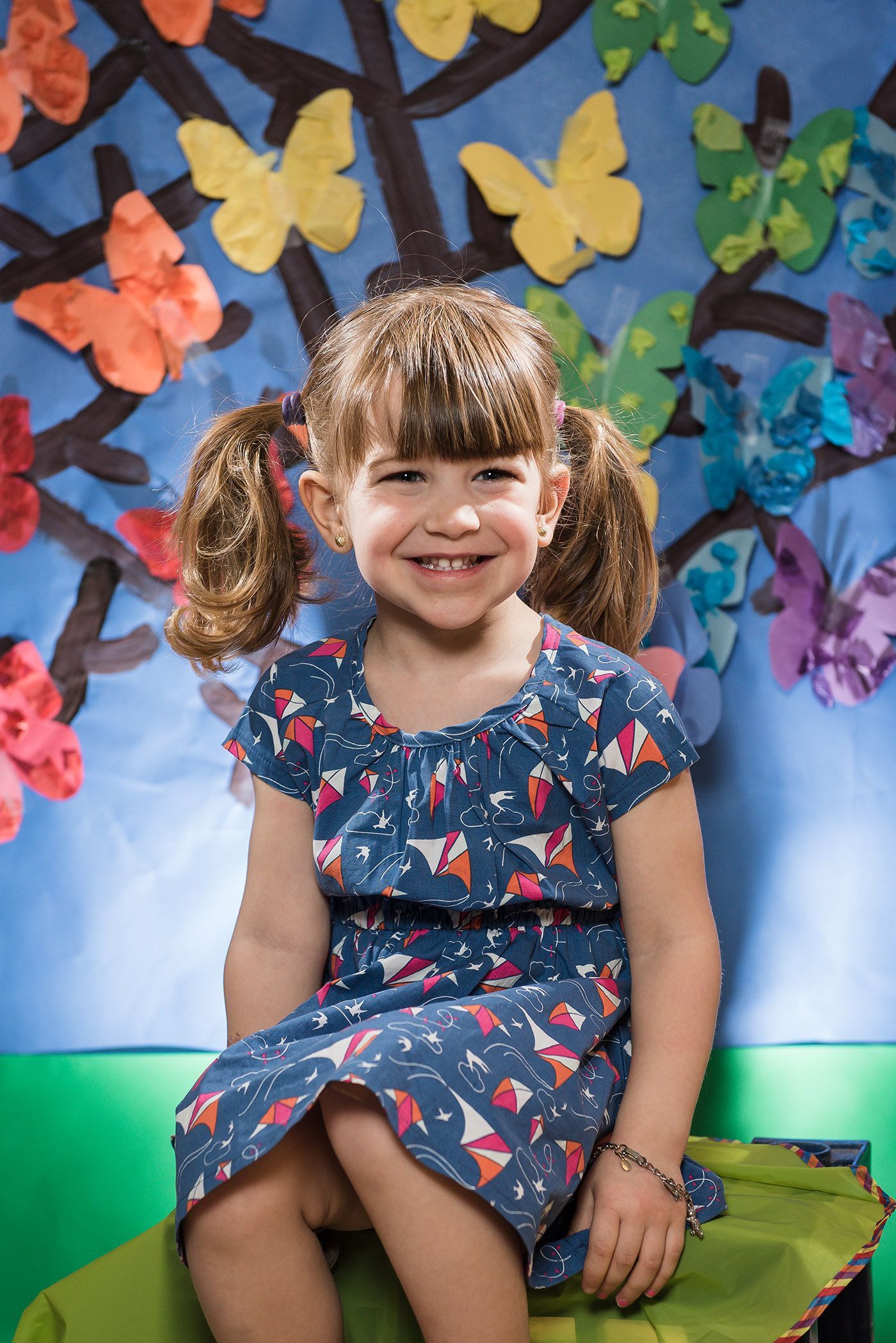 Child in floral dress sits under colorful paper butterfly decorations in playful setting.