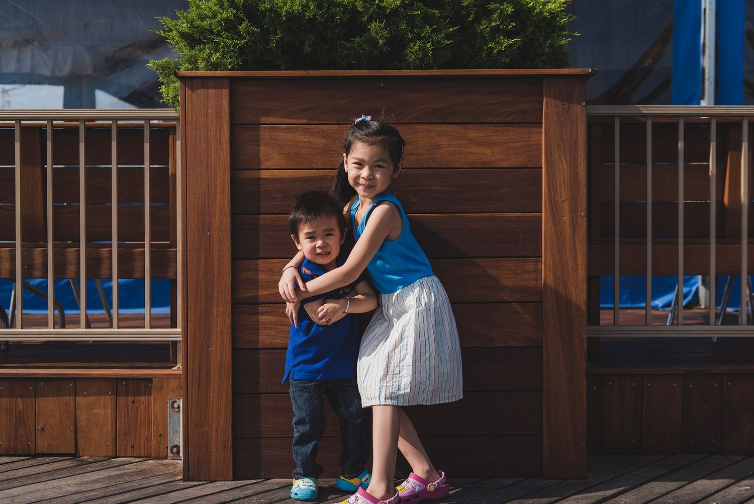 Child plays outside wooden building with blue trim in casual setting.