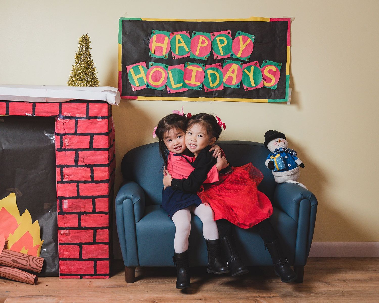 Holiday photo setup with blue couch and festive decorations against brick-colored wall backdrop.
