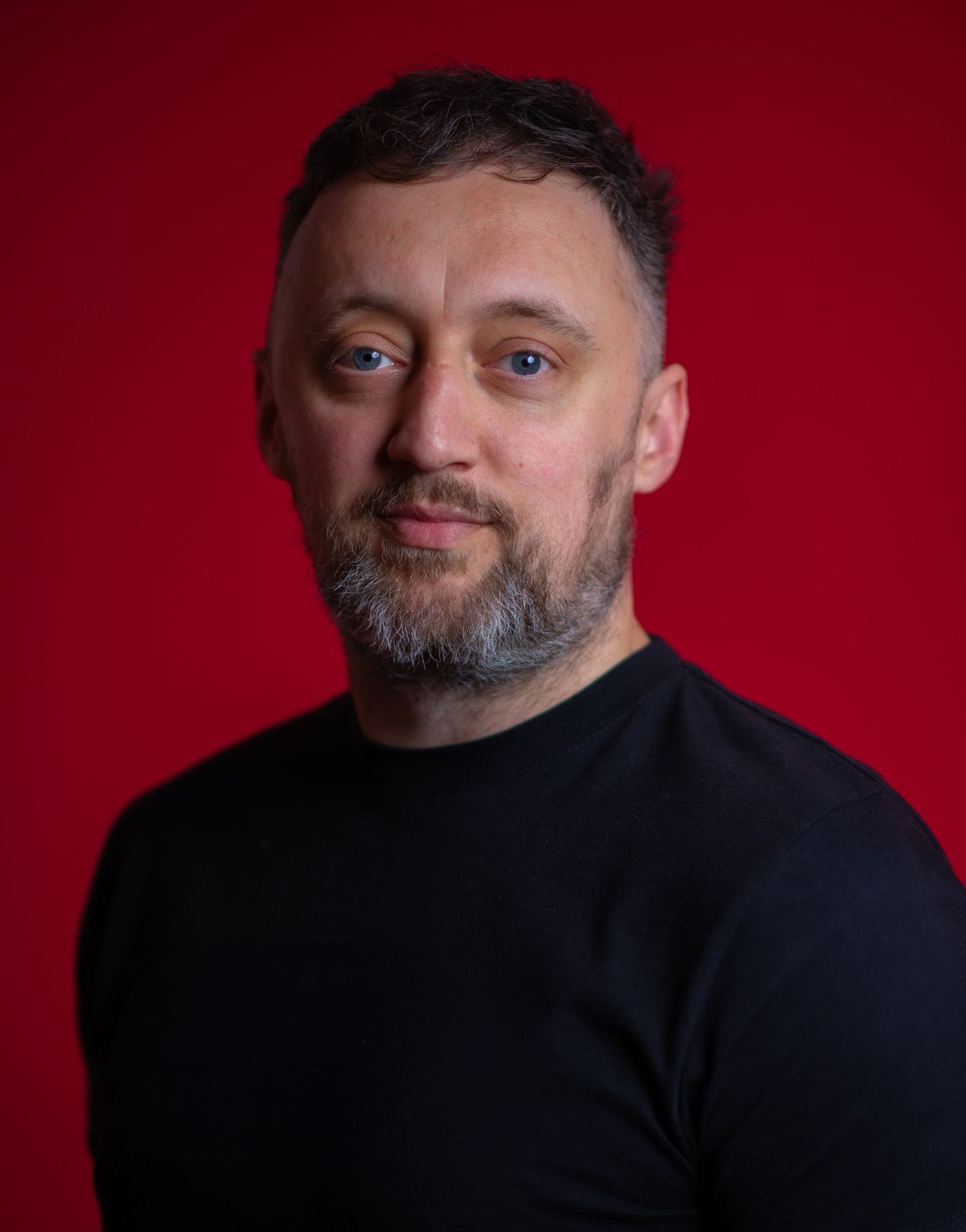 Glasgow creative headshot of a man in his thirties with short, dark hair and a black top in front of a vivid red backdrop