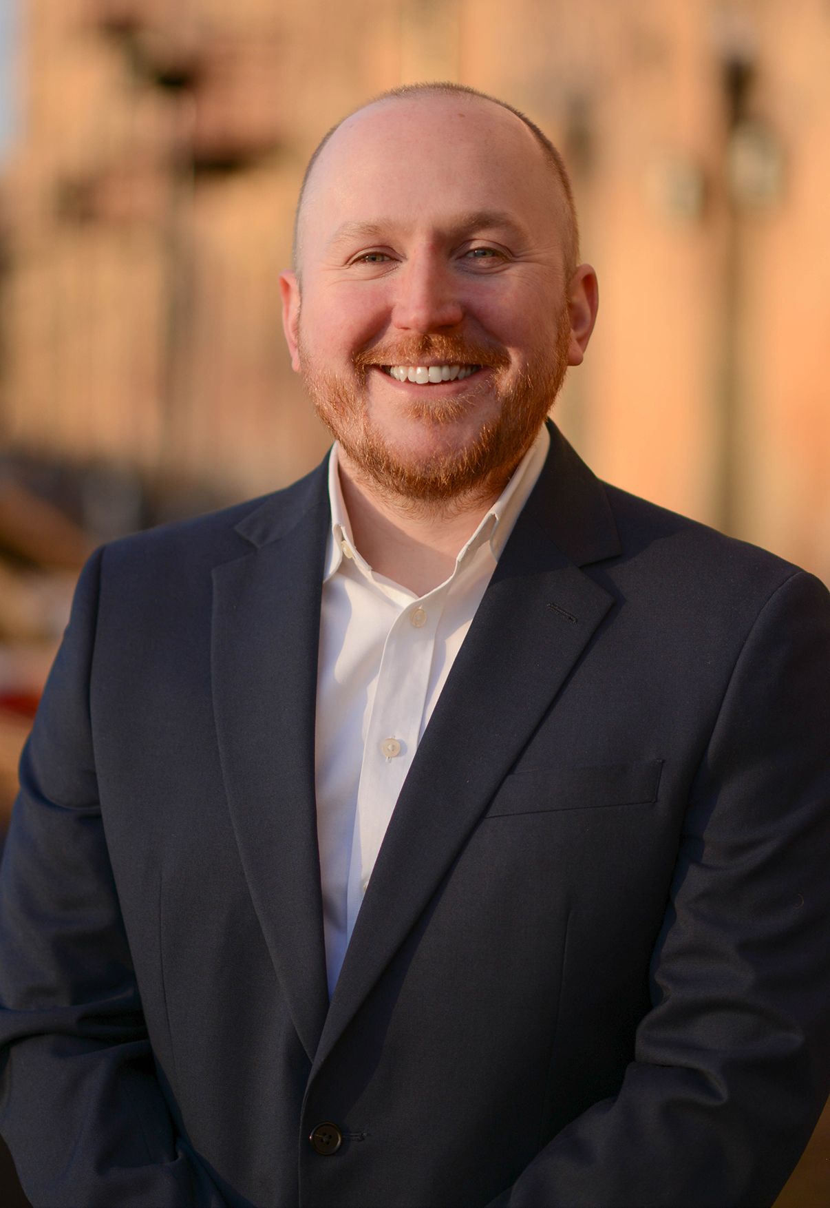 Glasgow corporate headshot of a bald man in his thirties with a black suit and white shirt, with a background of yellow sandstone flats