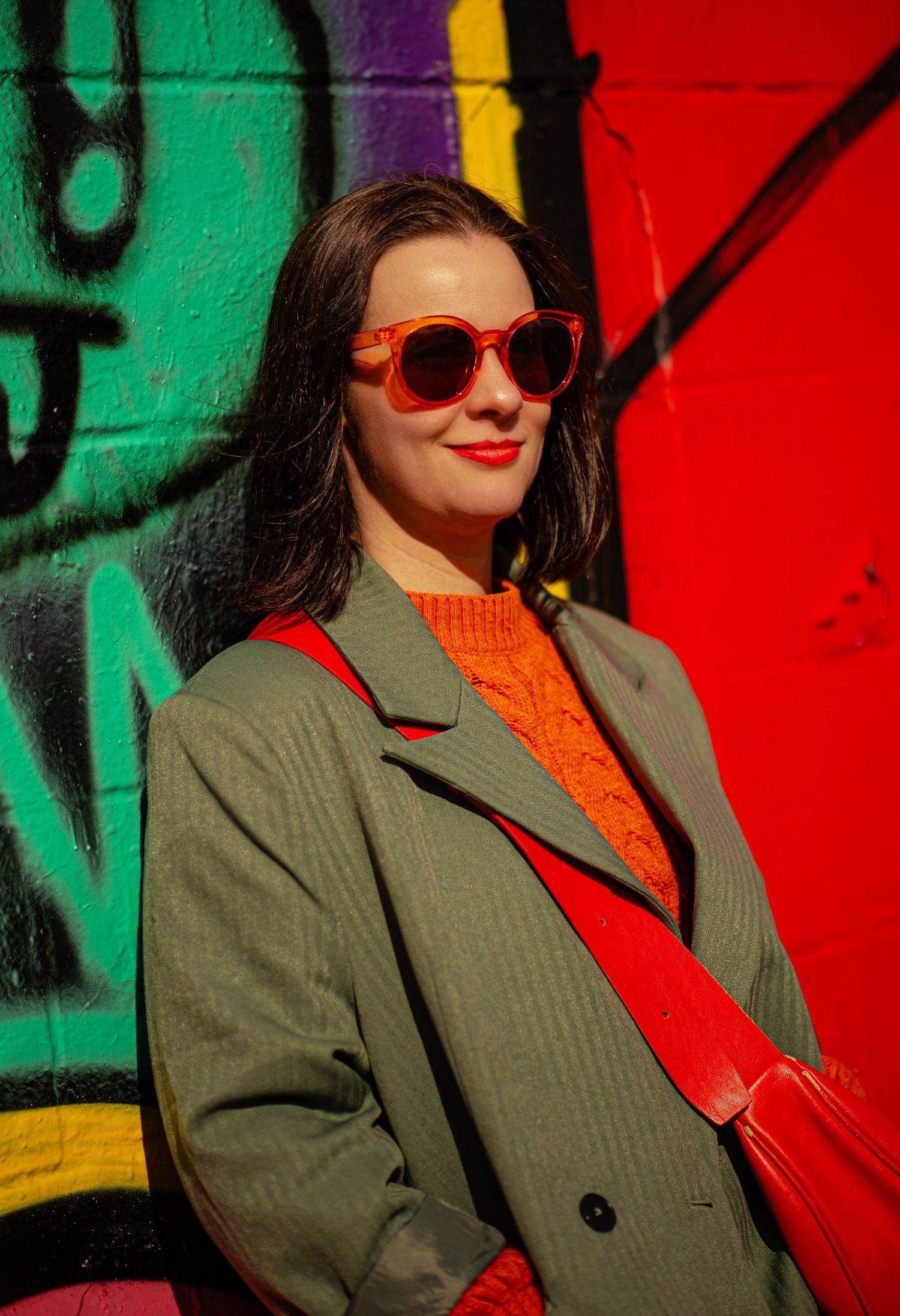 Glasgow creative portrait of a woman in her thirties with shoulder length black hair leaning on a wall of colourful graffiti