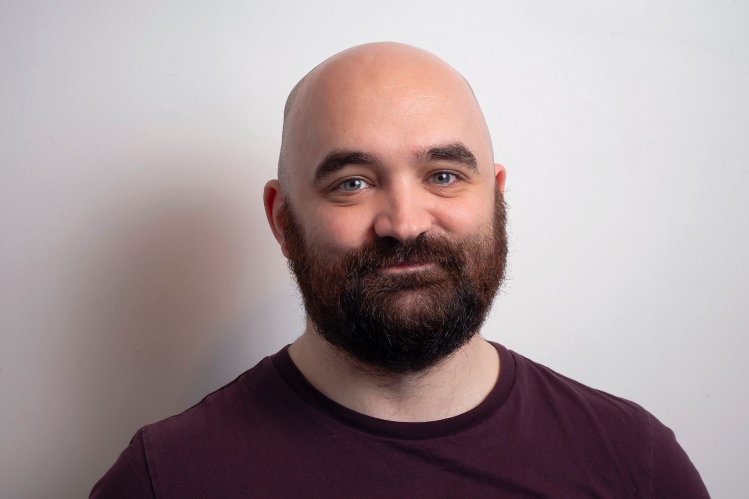 Glasgow corporate portrait of a smiling bald man with a beard wearing a dark red t-shirt against a white background