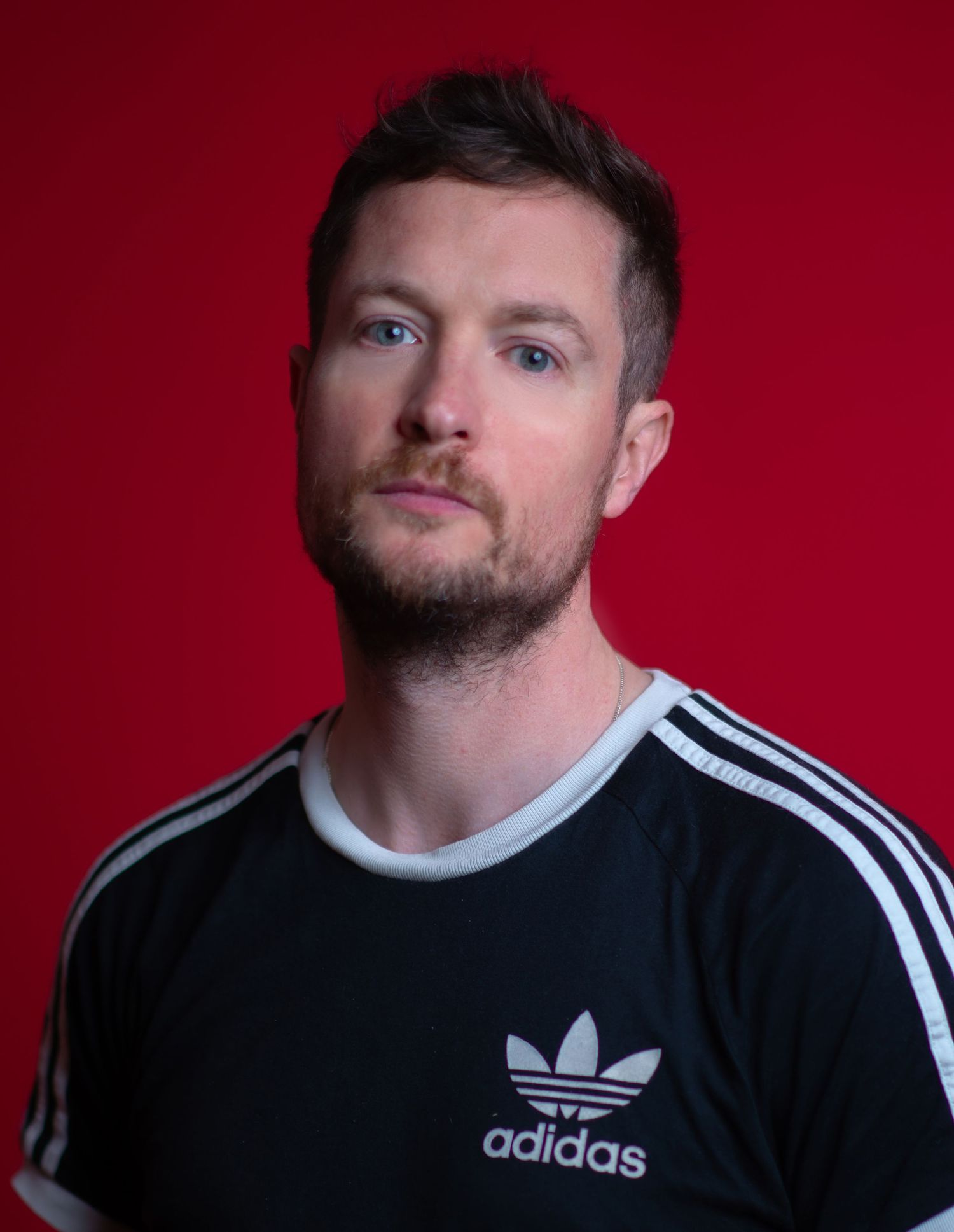 Glasgow creative headshot of a man in his thirties with short, dark hair and an adidas t-shirt in front of a vivid red backdrop