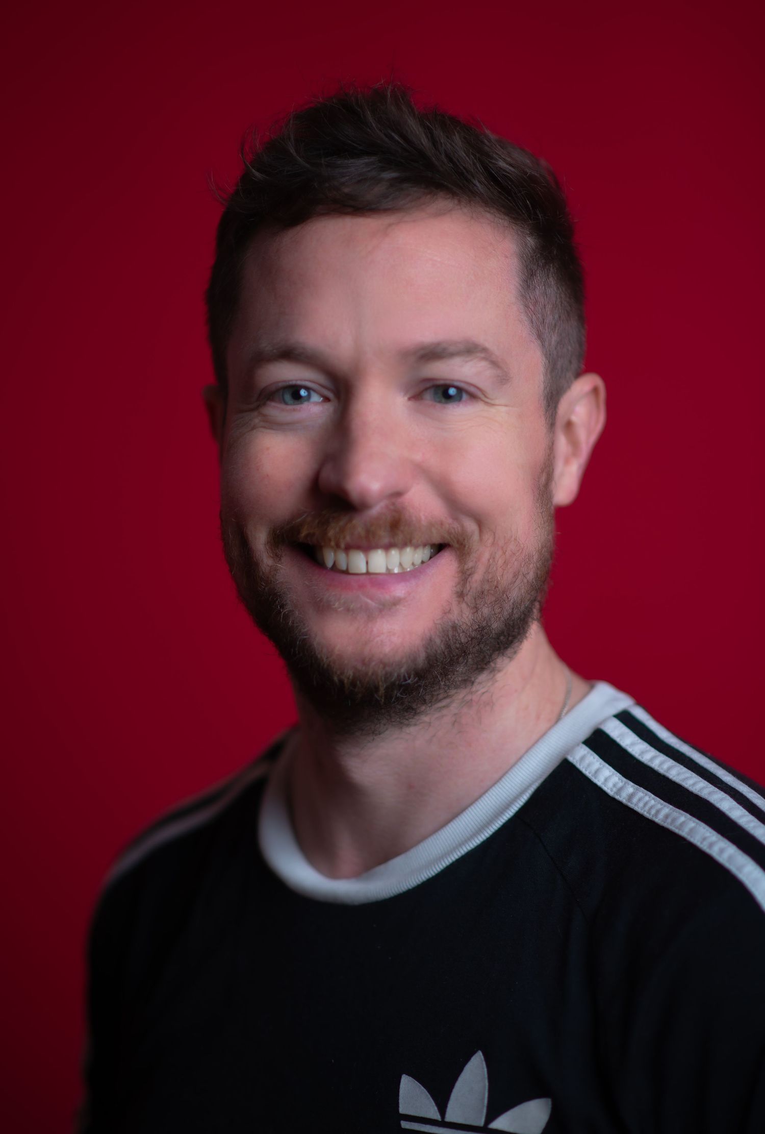 Glasgow corporate headshot of a smiling man in his thirties against a red background