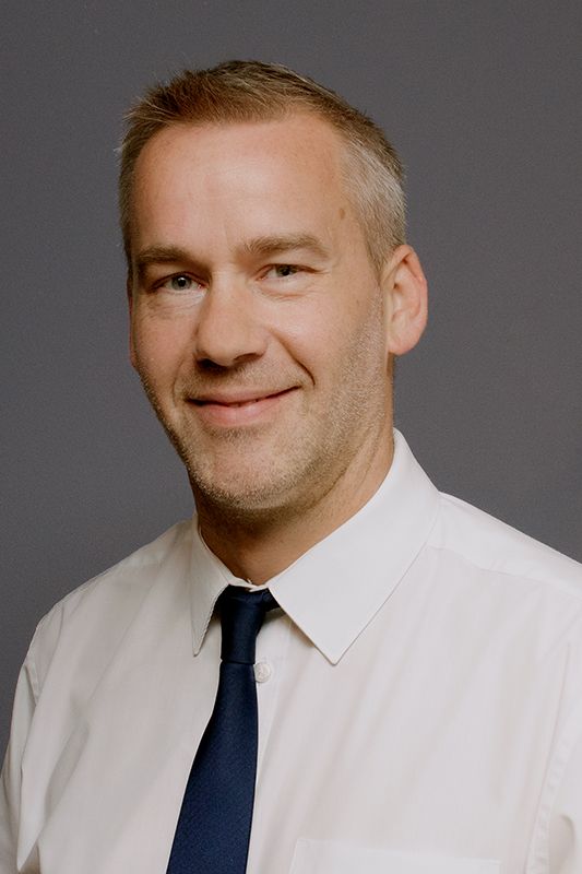 Glasgow corporate portrait of a short-haired man wearing a white shirt and dark tie against a dark grey background