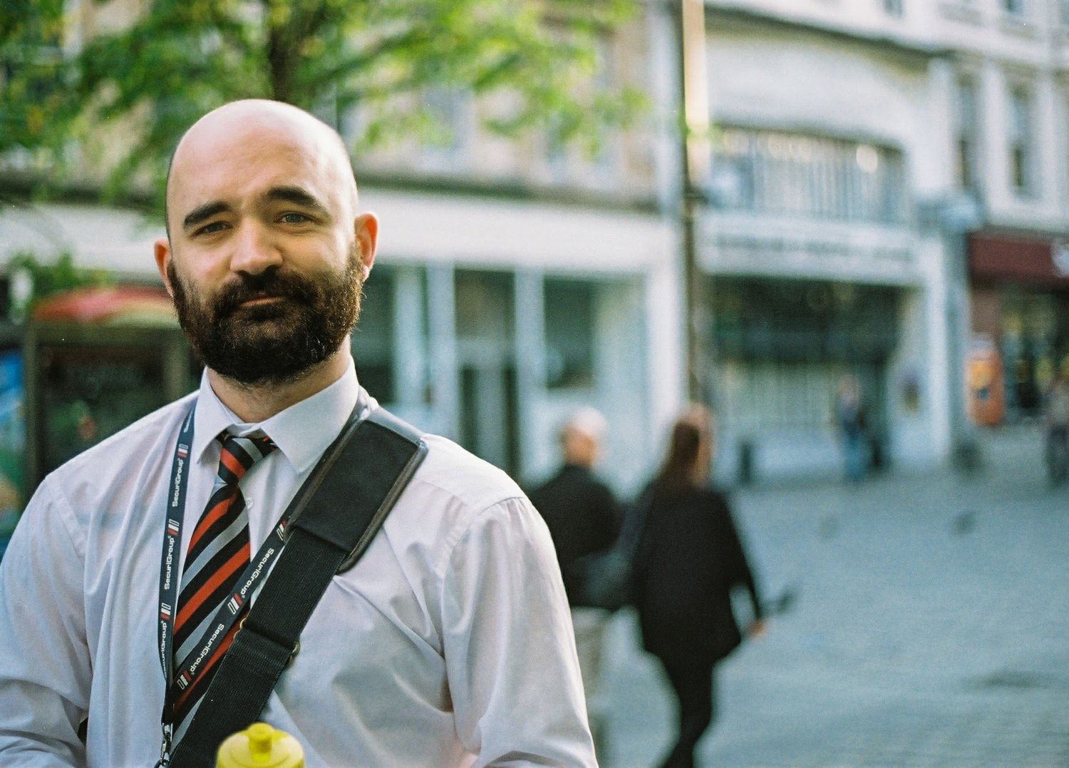Glasgow corporate portrait of a smiling bald man with a beard wearing a white shirt and striped tie against a high street background