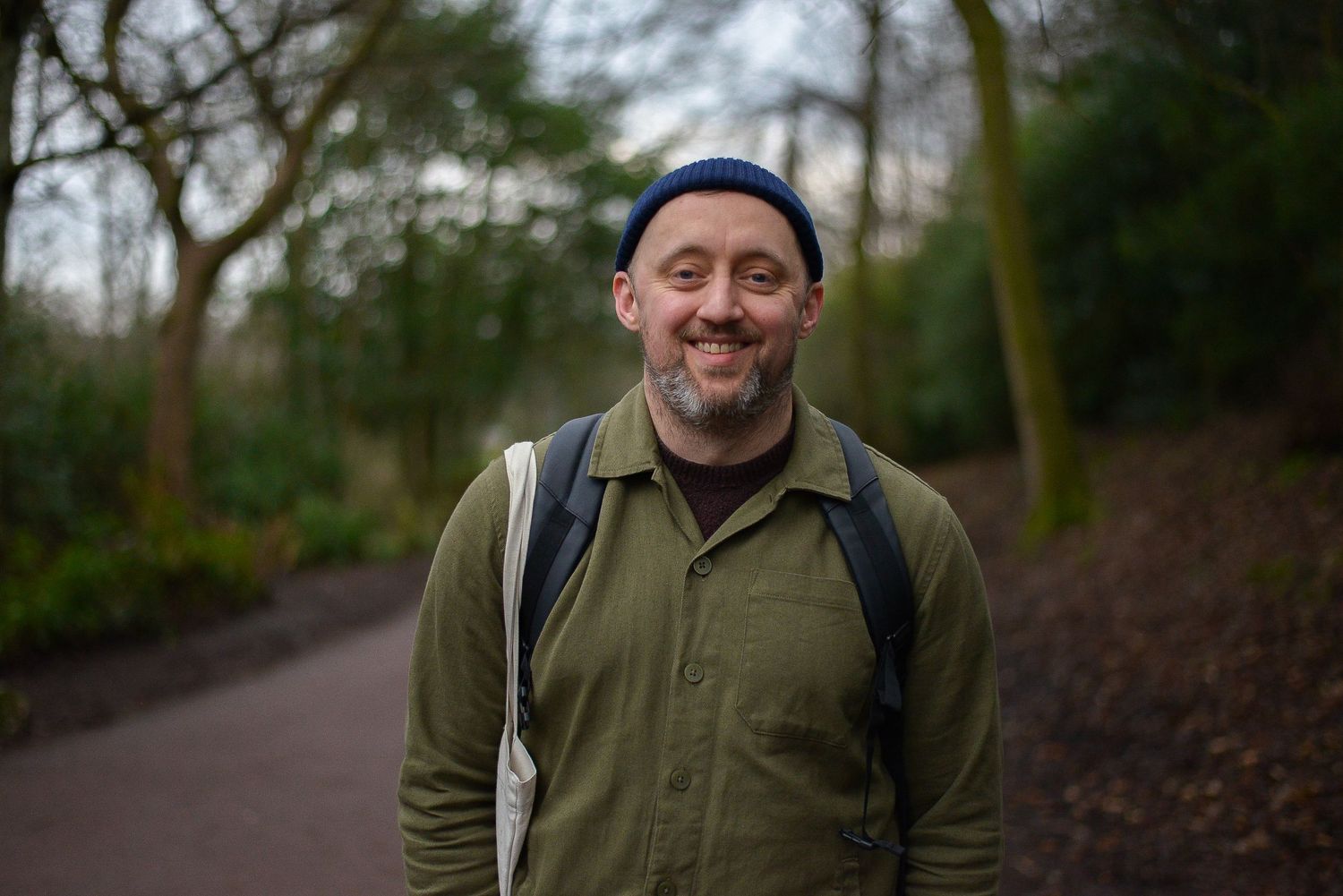 Corporate outdoor portrait of a smiling man in his thirties wearing a dark green shirt against a background of Glasgow park with trees