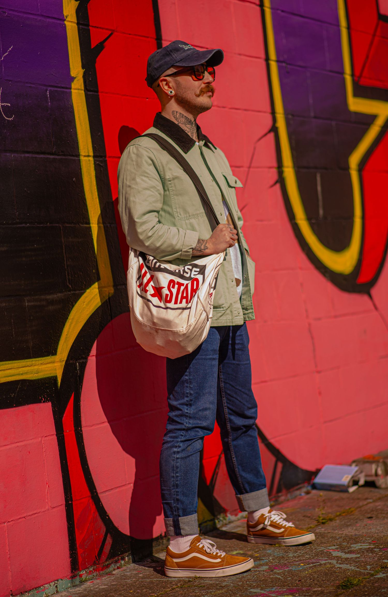 Glasgow creative portrait of a well-dressed man in his thirties with a tote bag leaning on a wall of colourful graffiti