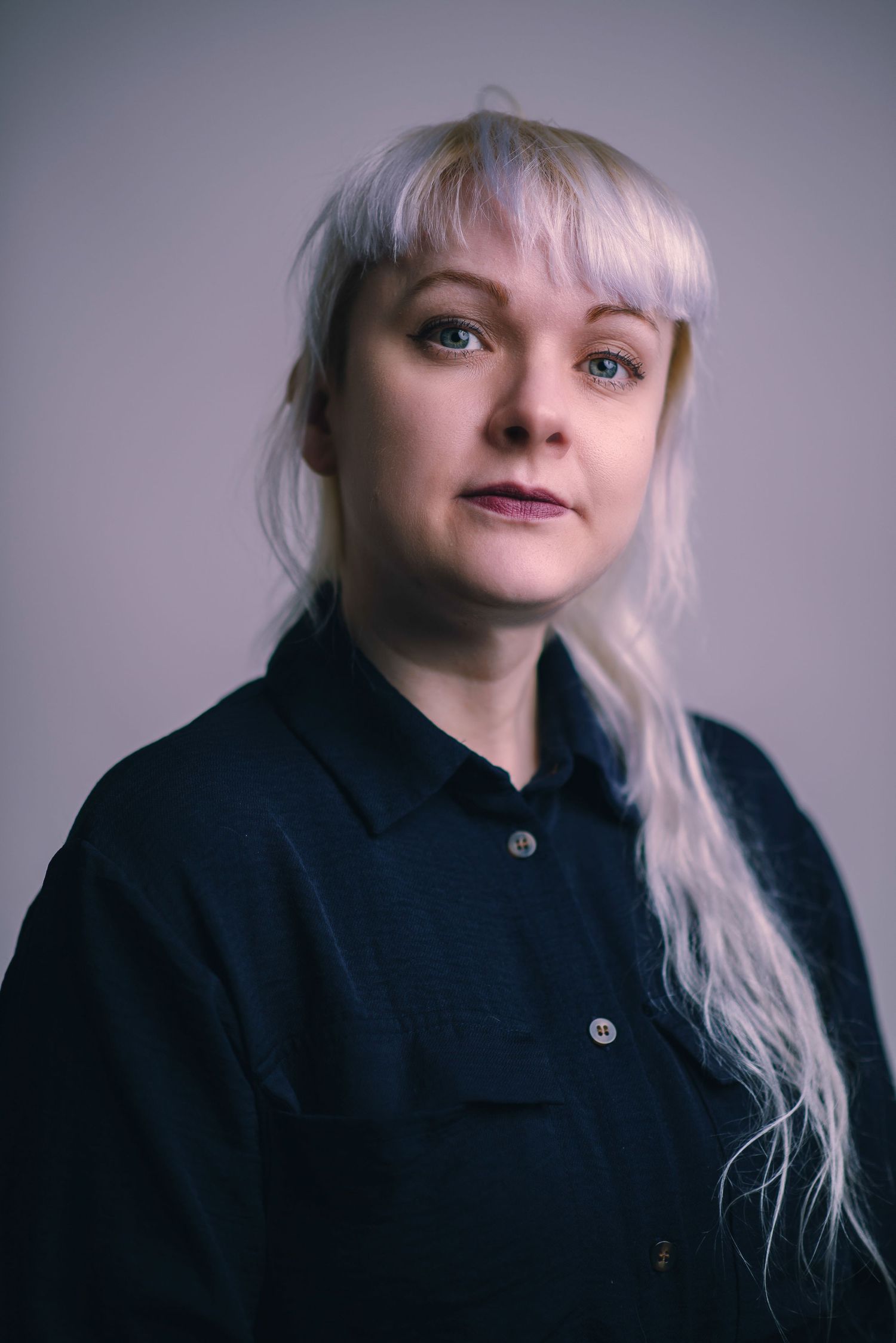 Glasgow corporate headshot of a woman in her thirties with white hair and a dark navy dress against a white background