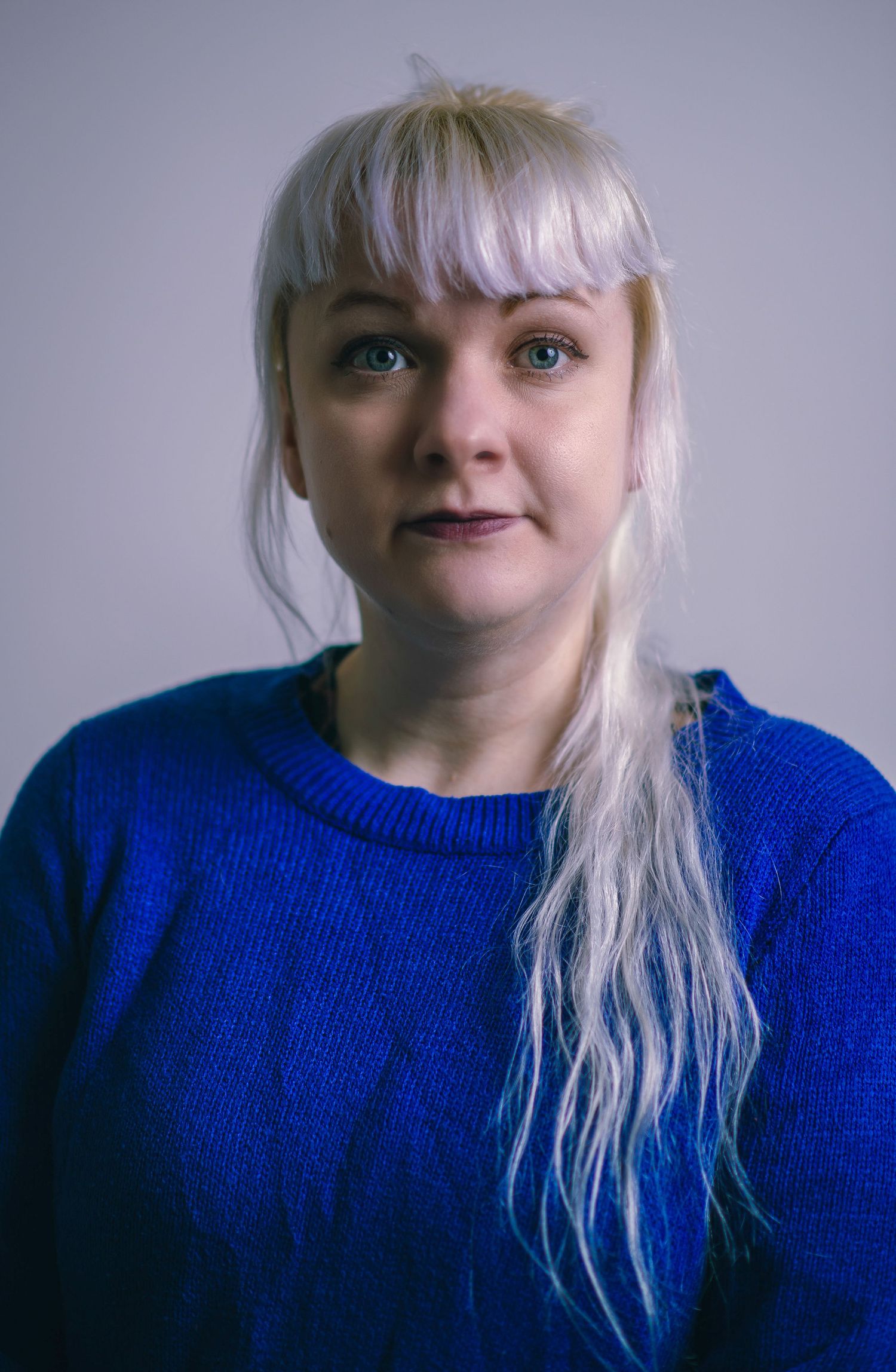 Glasgow corporate headshot of a woman in her thirties with white hair and a blue jumper against a white background