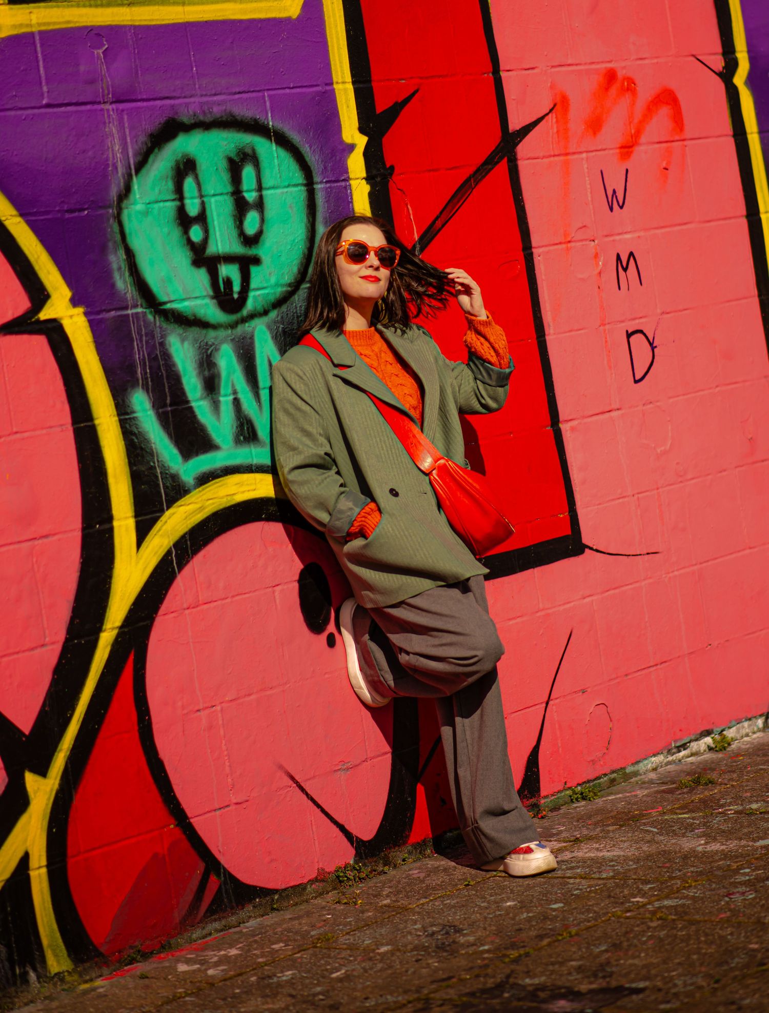 Glasgow creative portrait of a woman in her thirties with shoulder length black hair leaning on a wall of colourful graffiti