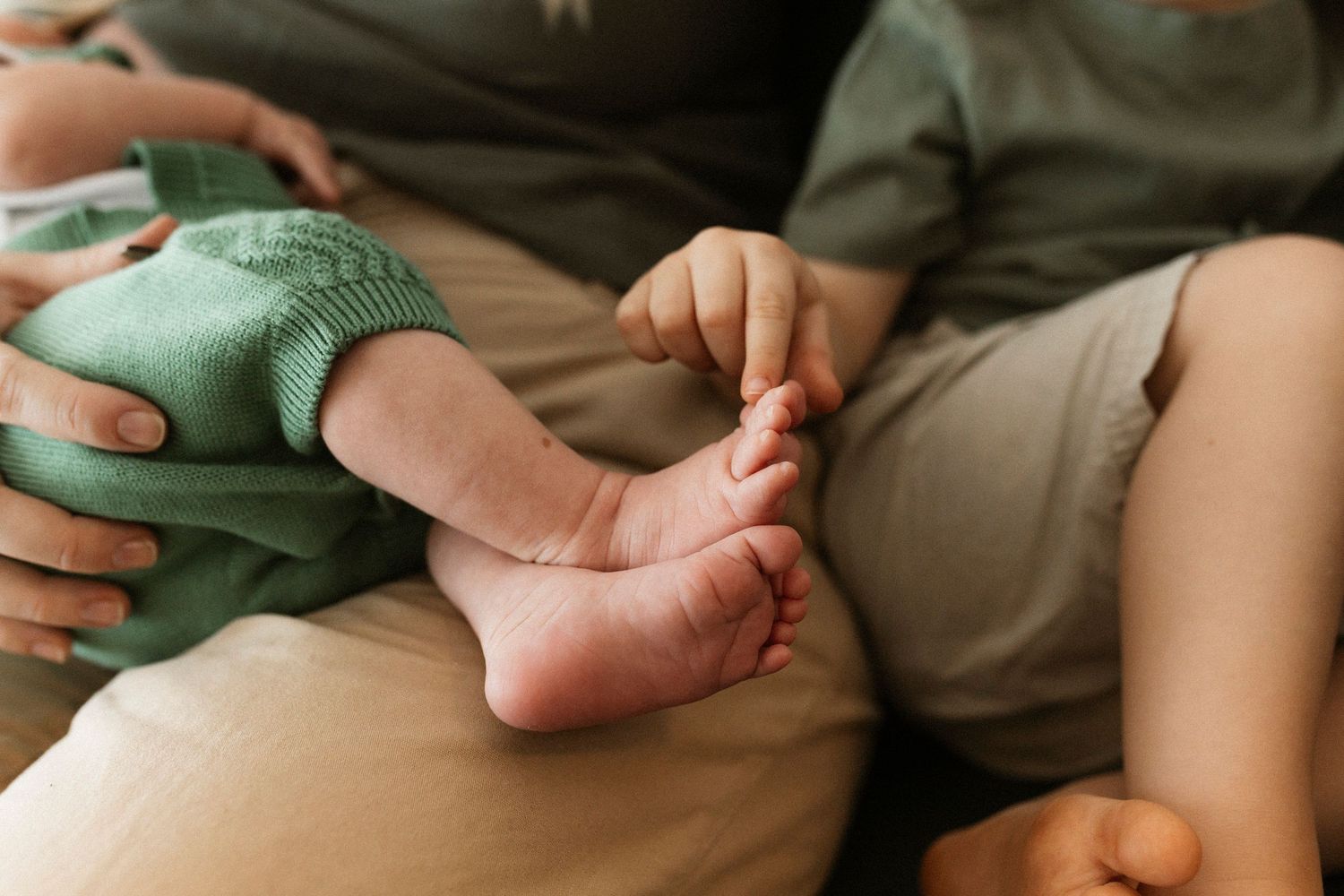 Close-up details of small children's feet and clothing on white bedding.
