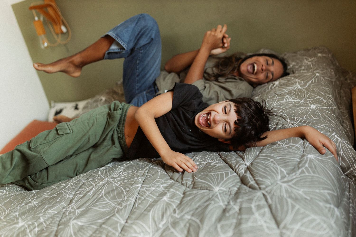 Playful moments captured on a comfortable grey bed with natural lighting.