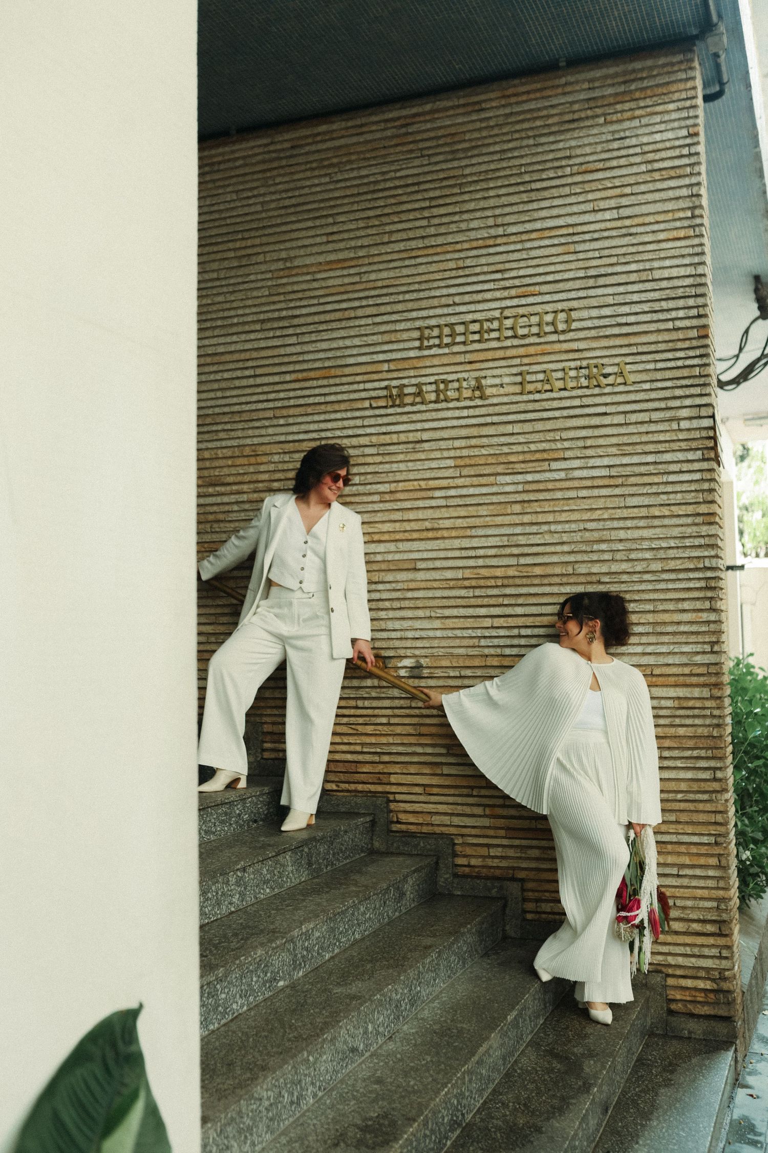 A person in white clothing poses artistically against a wall with rolling shutter doors.