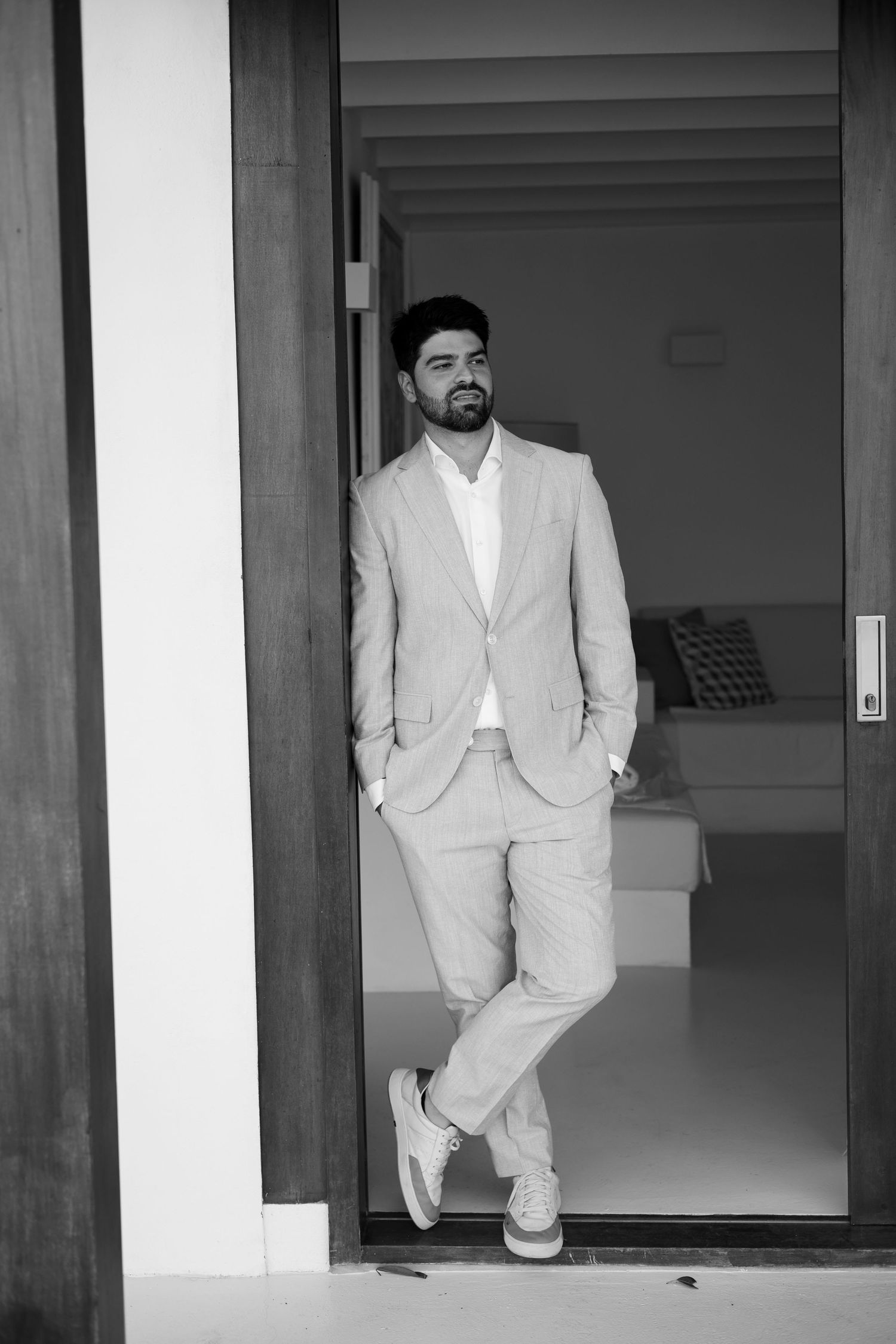 A figure in a white suit stands in an elegant hallway with wooden pillars.