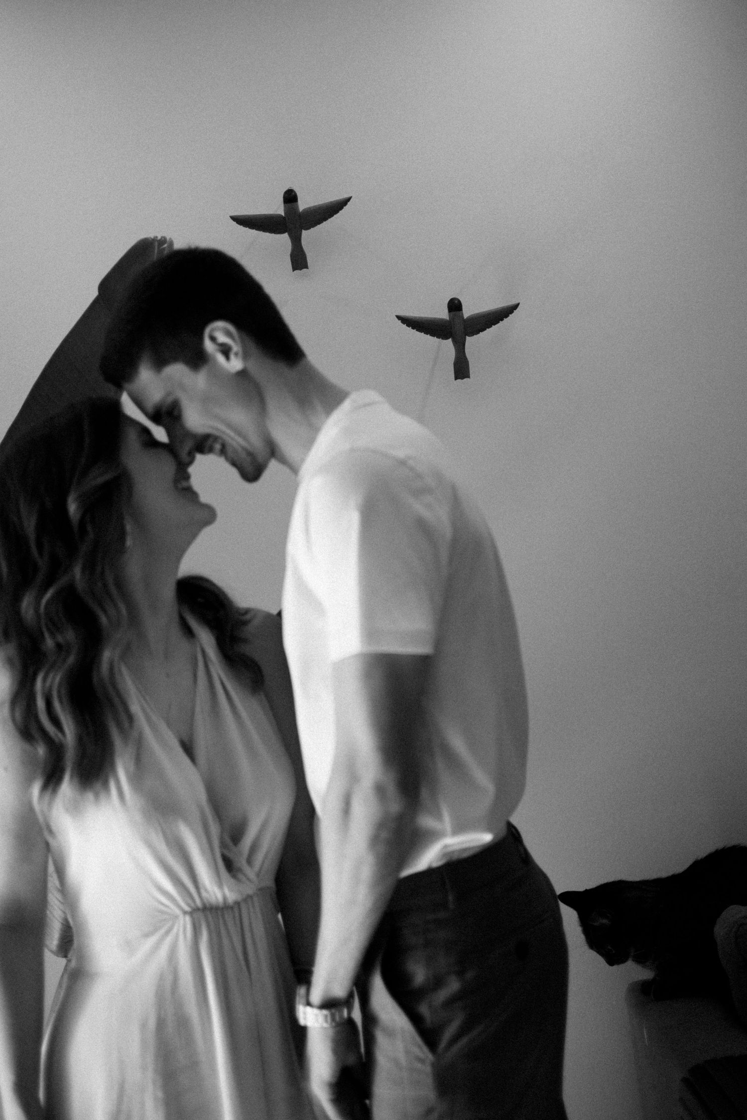 Artistic black and white photo of a couple in white clothing with birds flying in background.