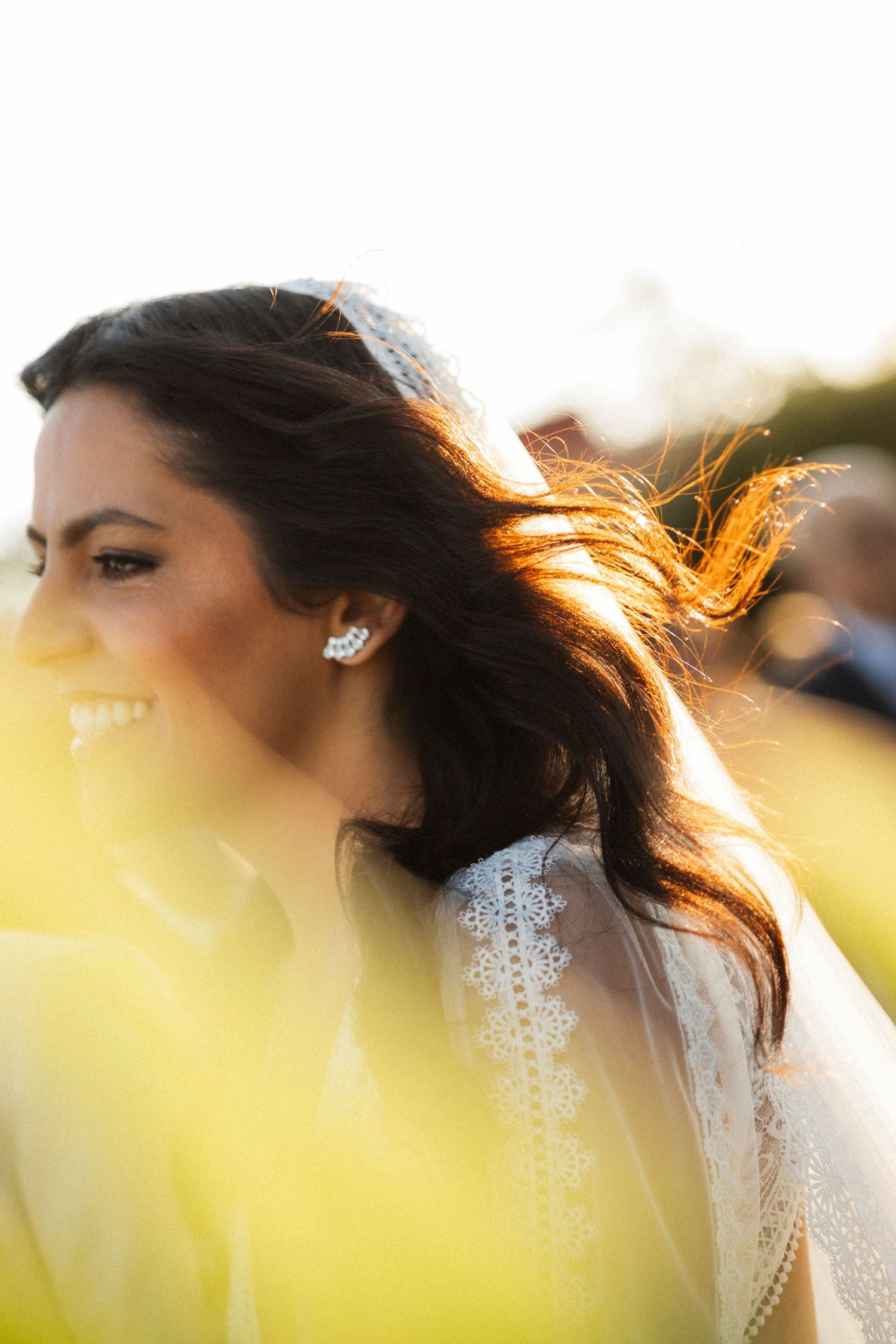 Bride's profile in golden sunlight highlighting intricate lace details of wedding dress.