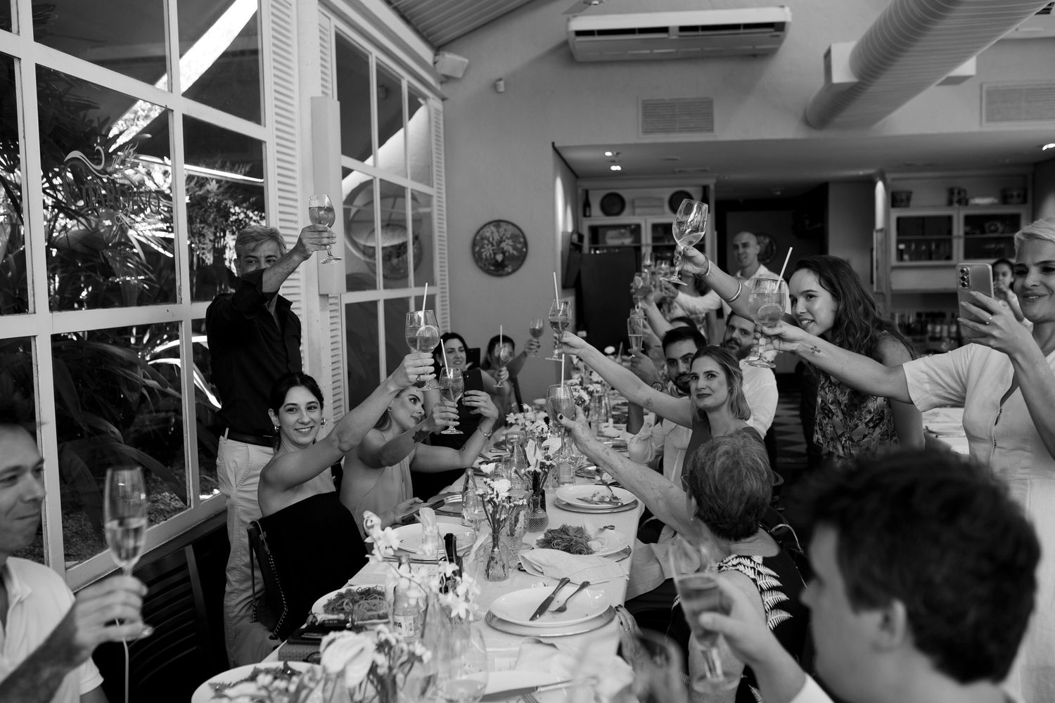 Wedding reception celebration with guests dining at long tables in a bright indoor venue.