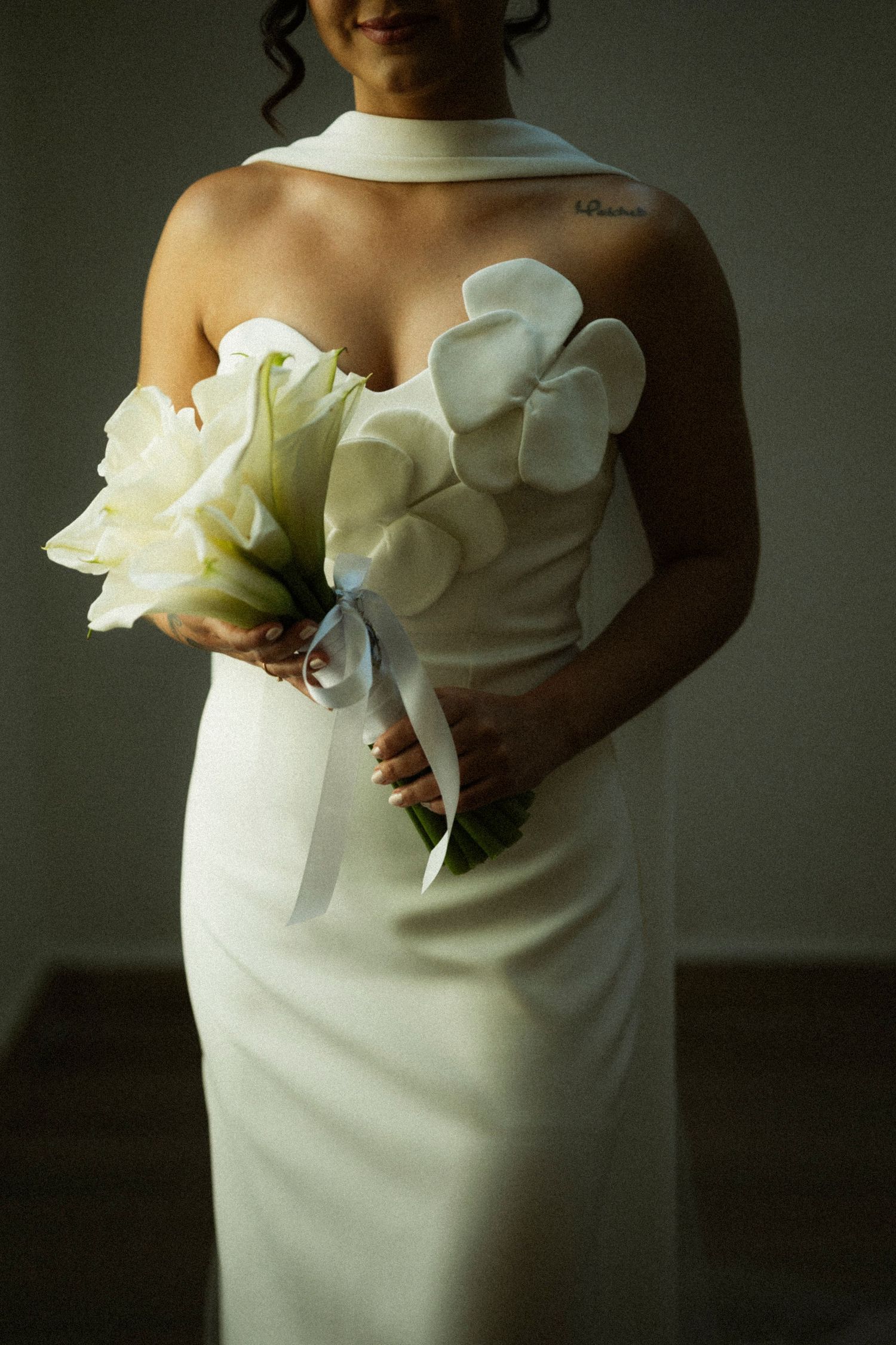 Bride in white strapless gown with floral appliques holding elegant white bouquet tied with blue ribbon.