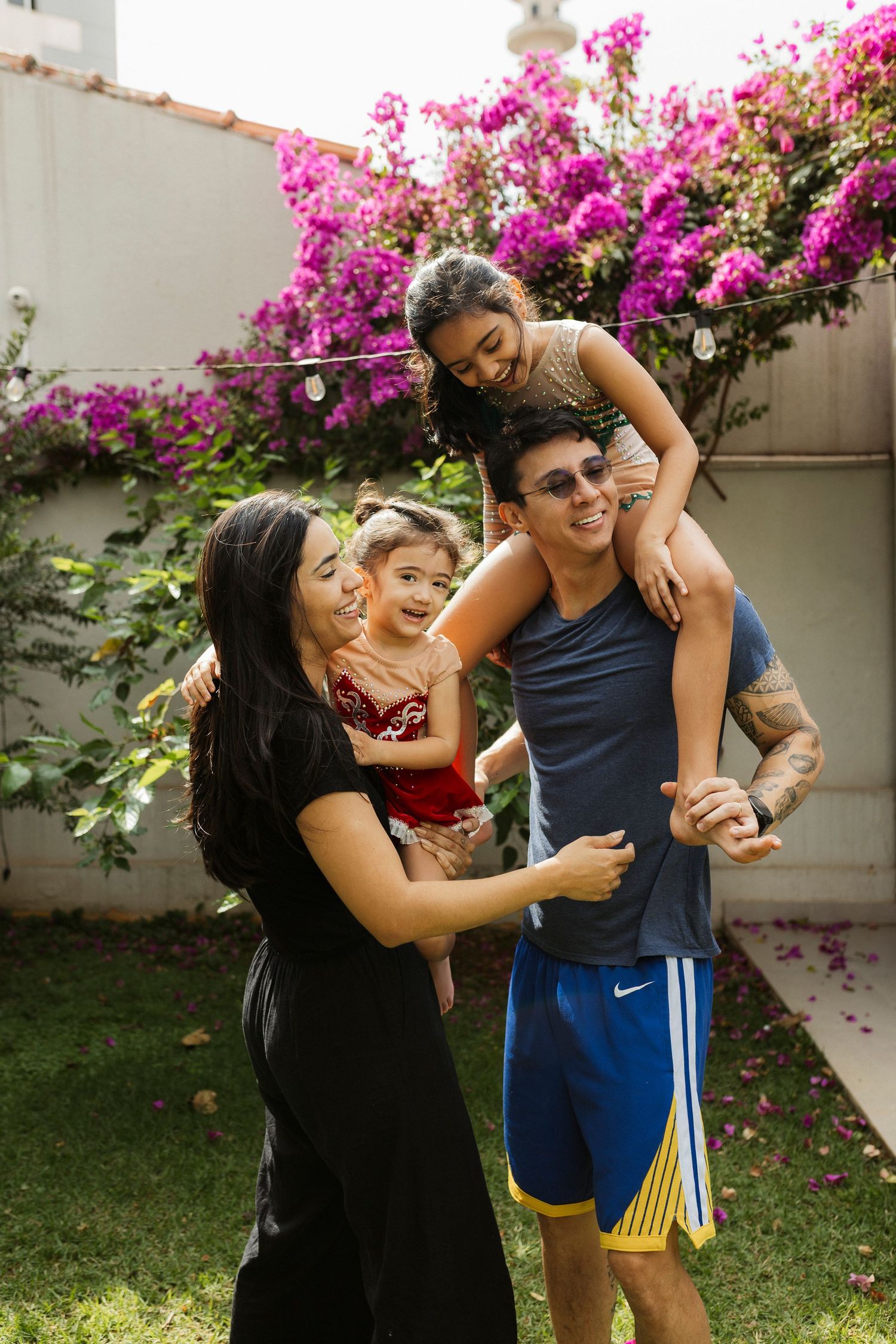 Happy family of four enjoying outdoor time with vibrant pink bougainvillea flowers in background.