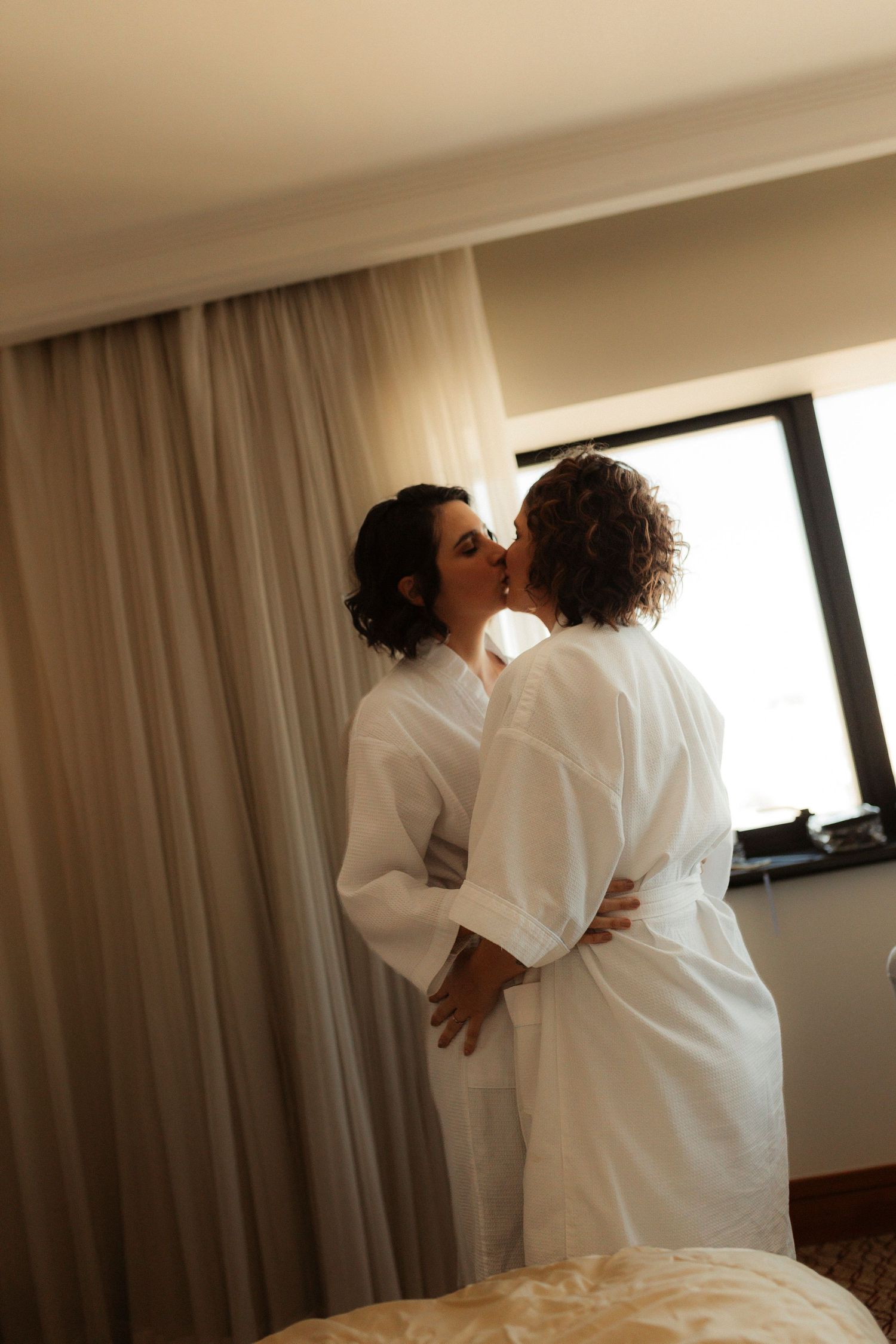 Intimate sequence in white robes by window with soft natural lighting.