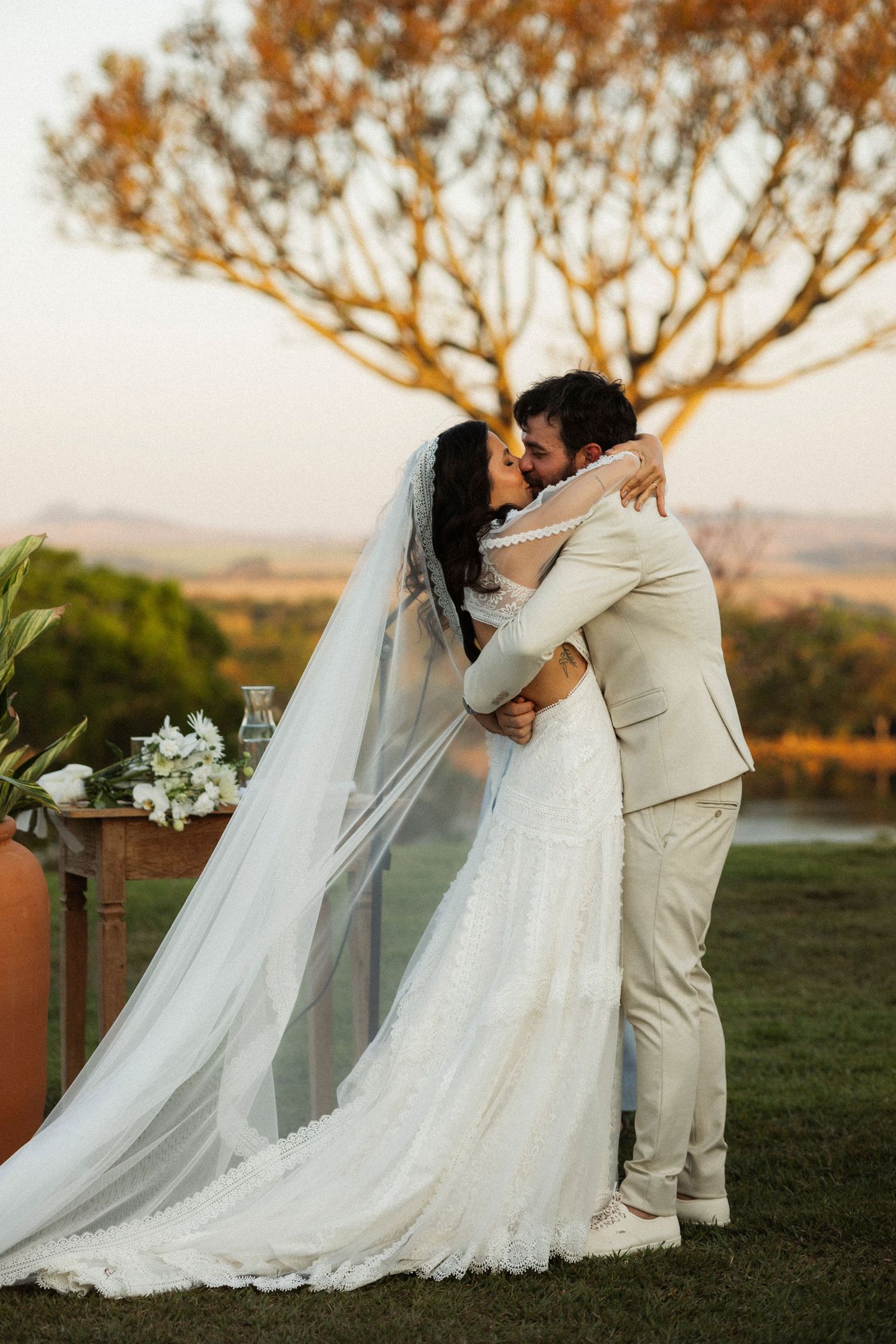 Romantic sunset wedding portraits with flowing veil and natural landscape backdrop.