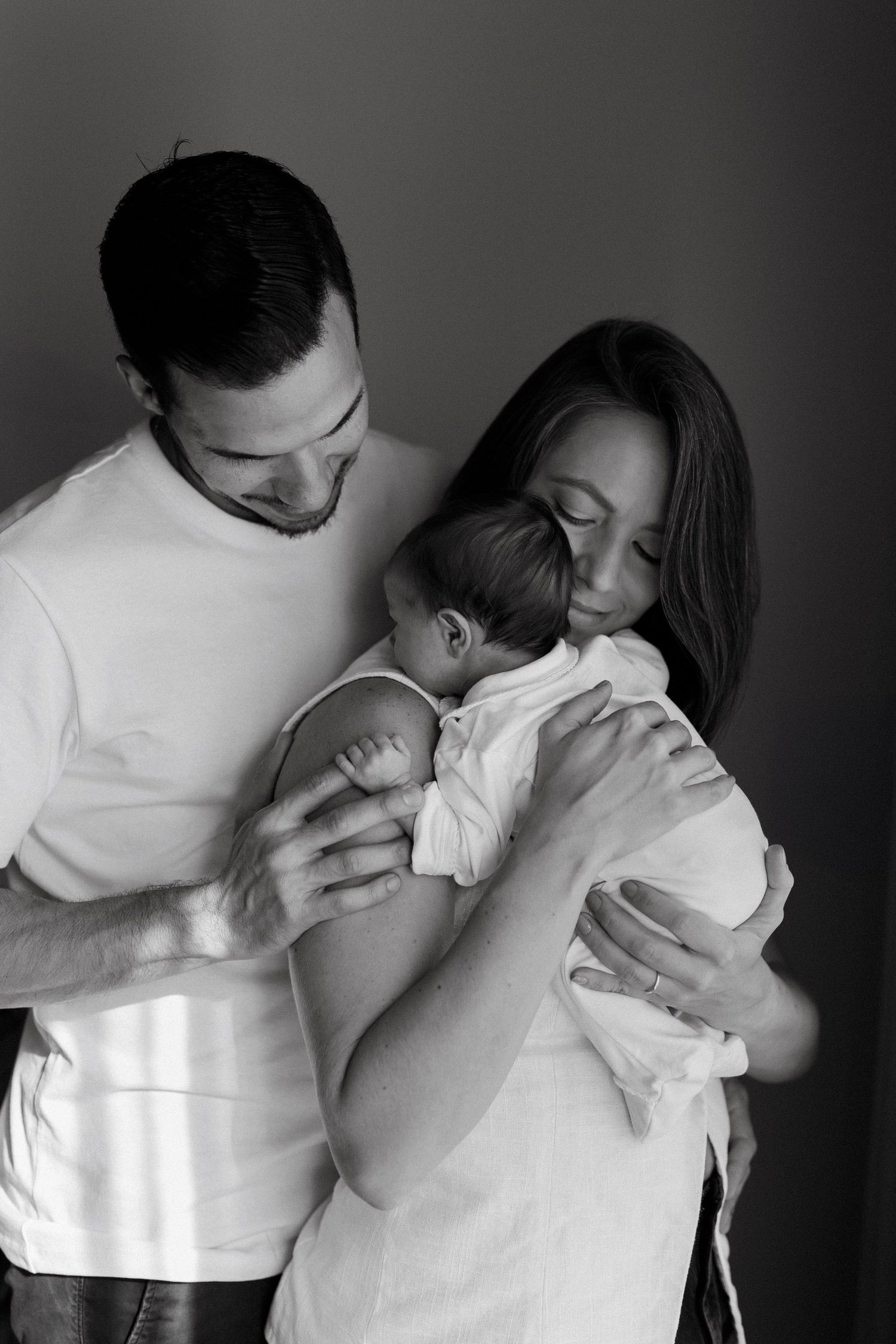 Black and white photo of parents lovingly holding their newborn baby close, sharing a tender family moment.