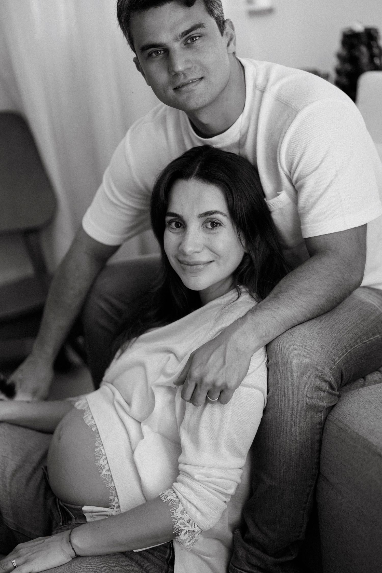 Black and white photo of a pregnant woman and her partner posing together on a couch at home.