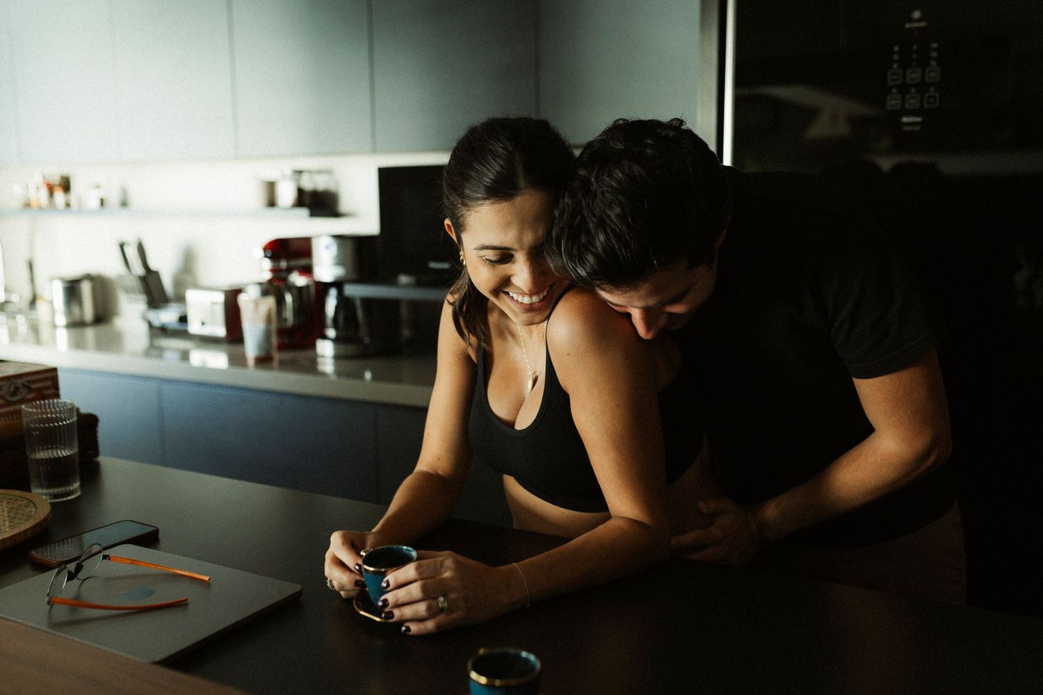 Couple sharing an intimate moment in a modern kitchen, smiling while looking at a small object together.