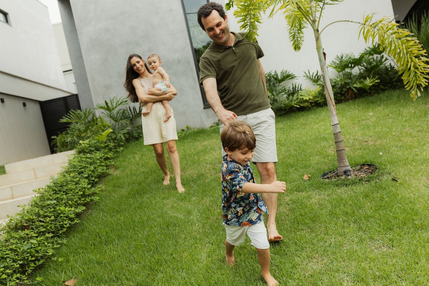 Family enjoying time together in a backyard garden with lush green grass and tropical plants.