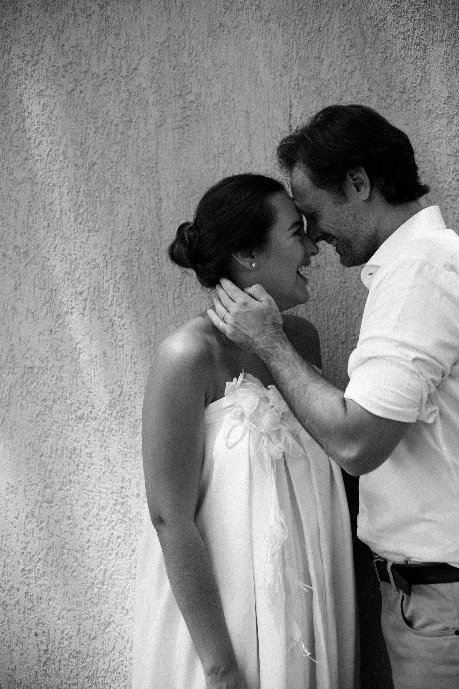 Black and white portrait captures an intimate moment between a couple against a textured wall.